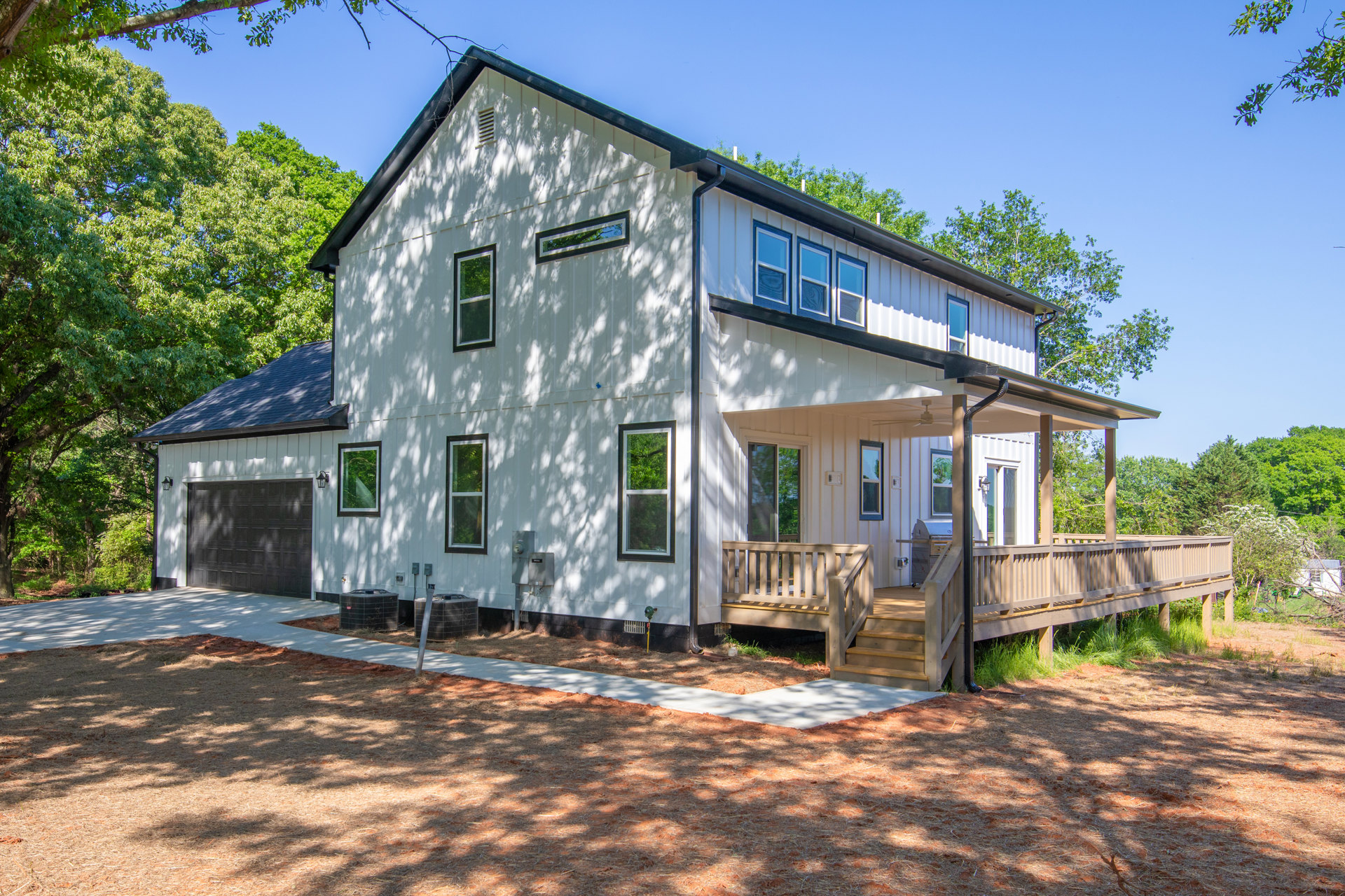 White siding house with attached garage, covered porch featuring a grill, white framed windows, green tree in background, landscaped front yard.