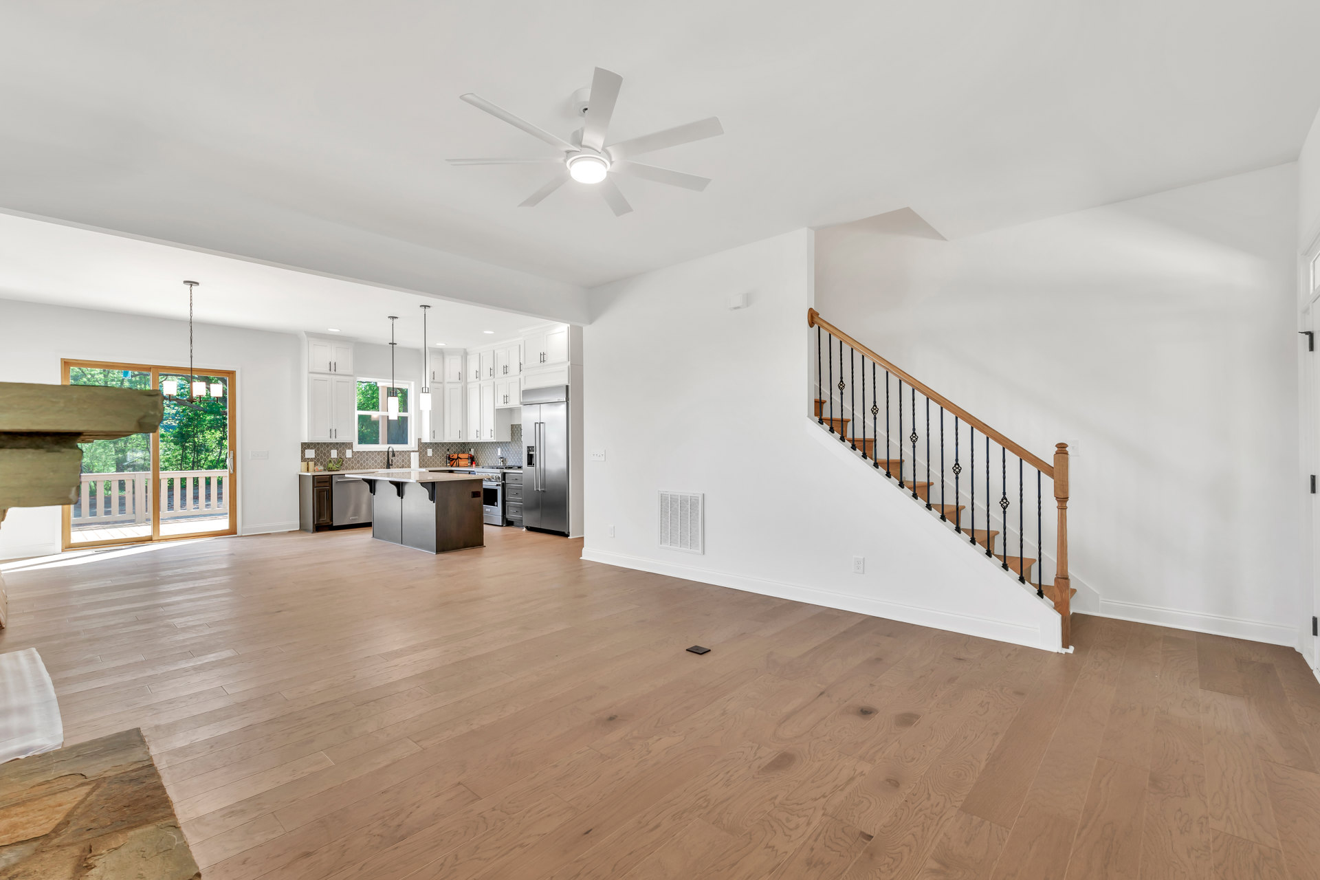 Open-concept living area featuring a wooden staircase with matching railings, wood flooring, white walls, a ceiling fan with light, and a kitchen island with a white countertop
