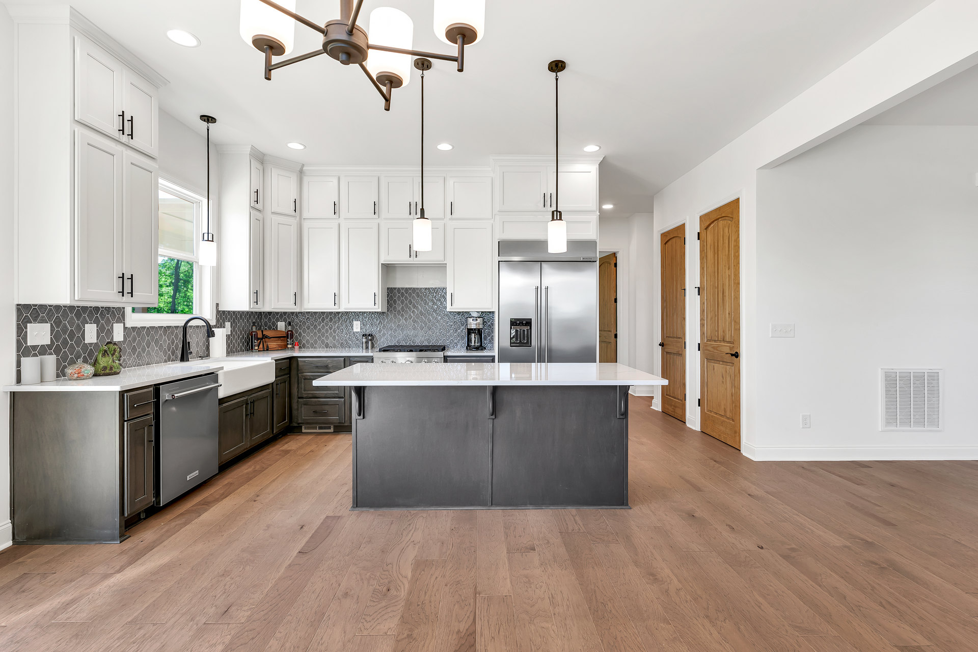 Spacious kitchen featuring a large white island with built-in sink, two-door stainless steel refrigerator, white countertops, light cabinetry, and hardwood flooring.