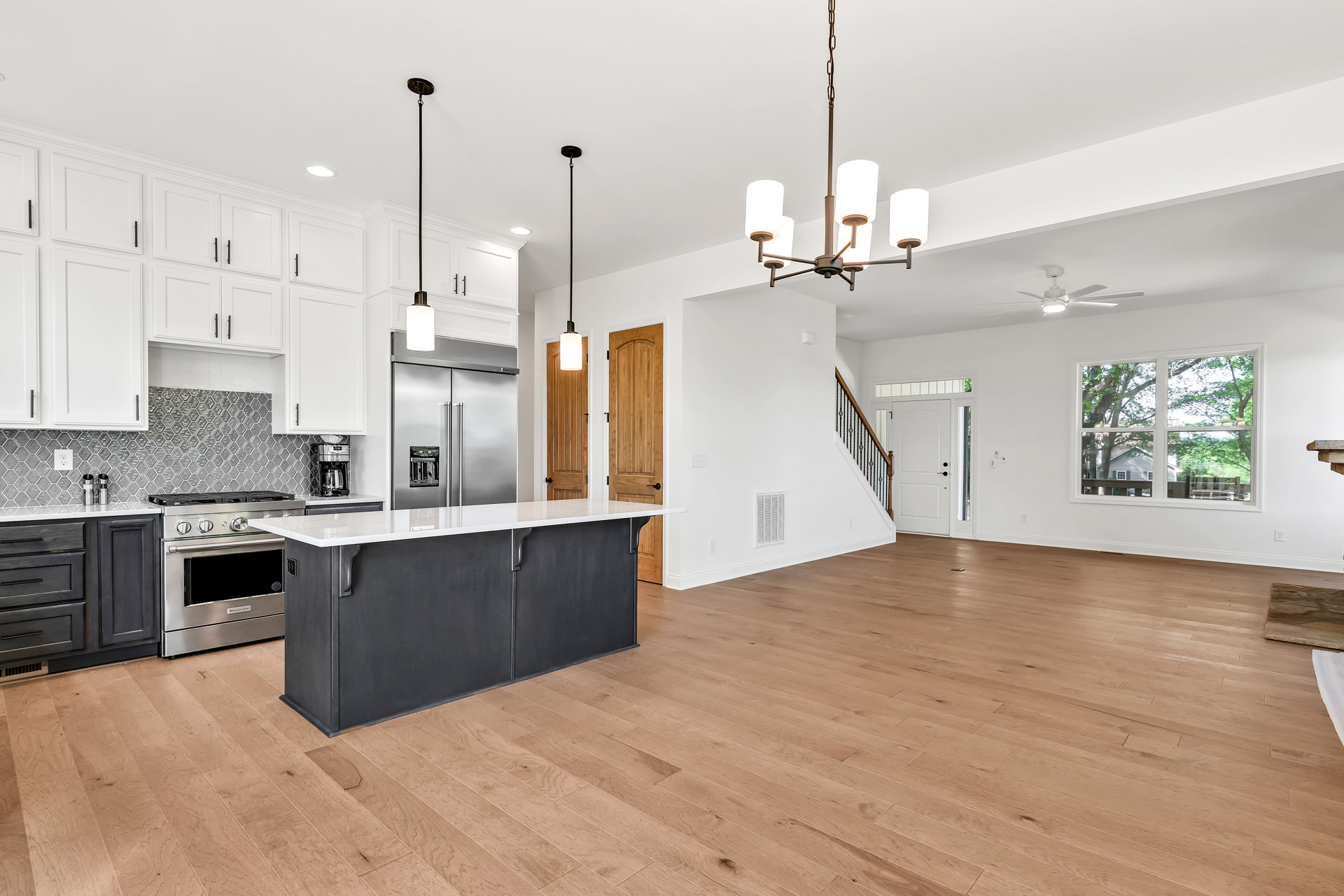 Open kitchen and living room with hardwood floors, white countertop, stainless steel stove and oven, light fixture, door, and drawer visible
