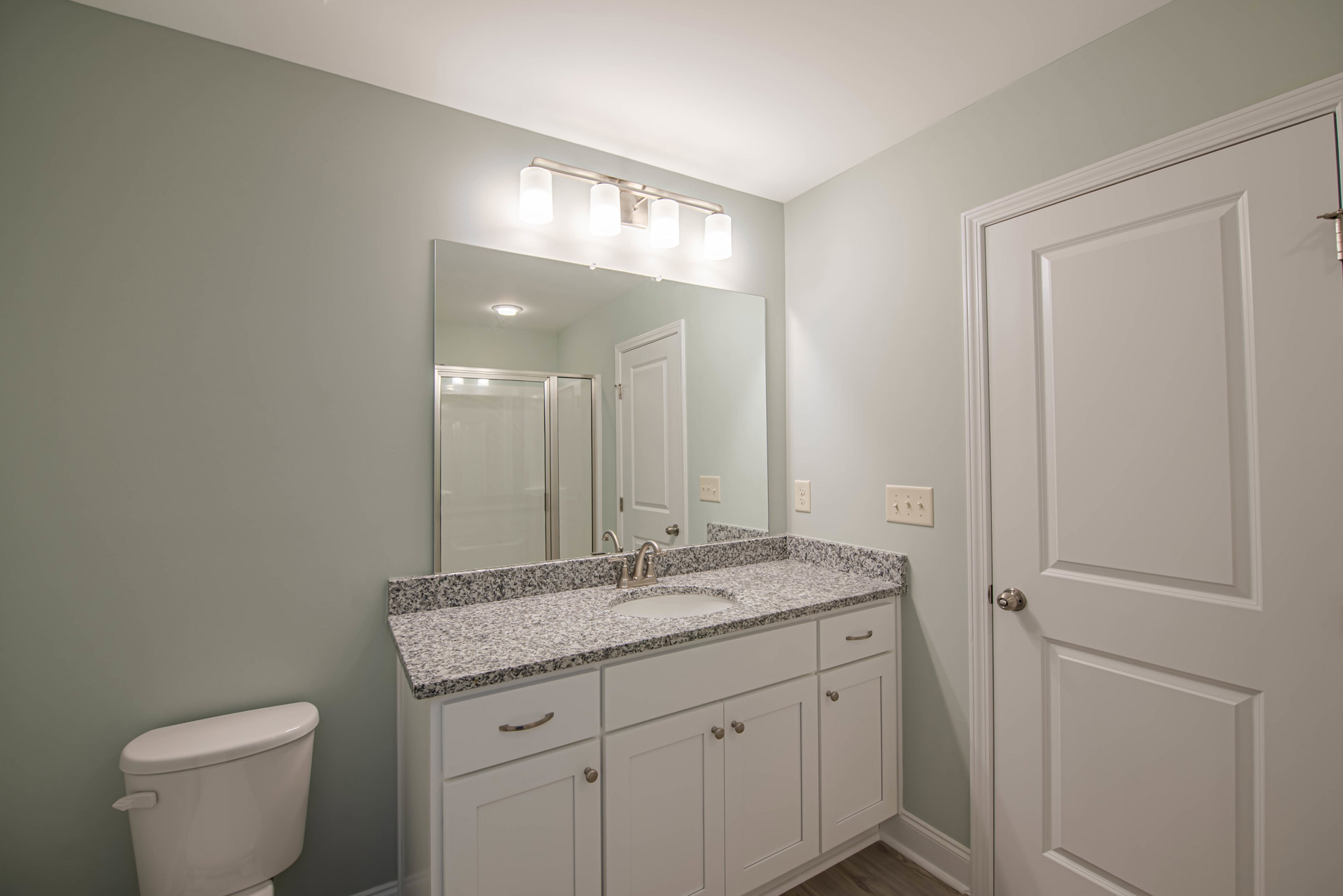 Modern bathroom featuring a rectangular sink with chrome faucet, large frameless mirror above, white toilet with silver handle, glass shower door with white frame, white door with