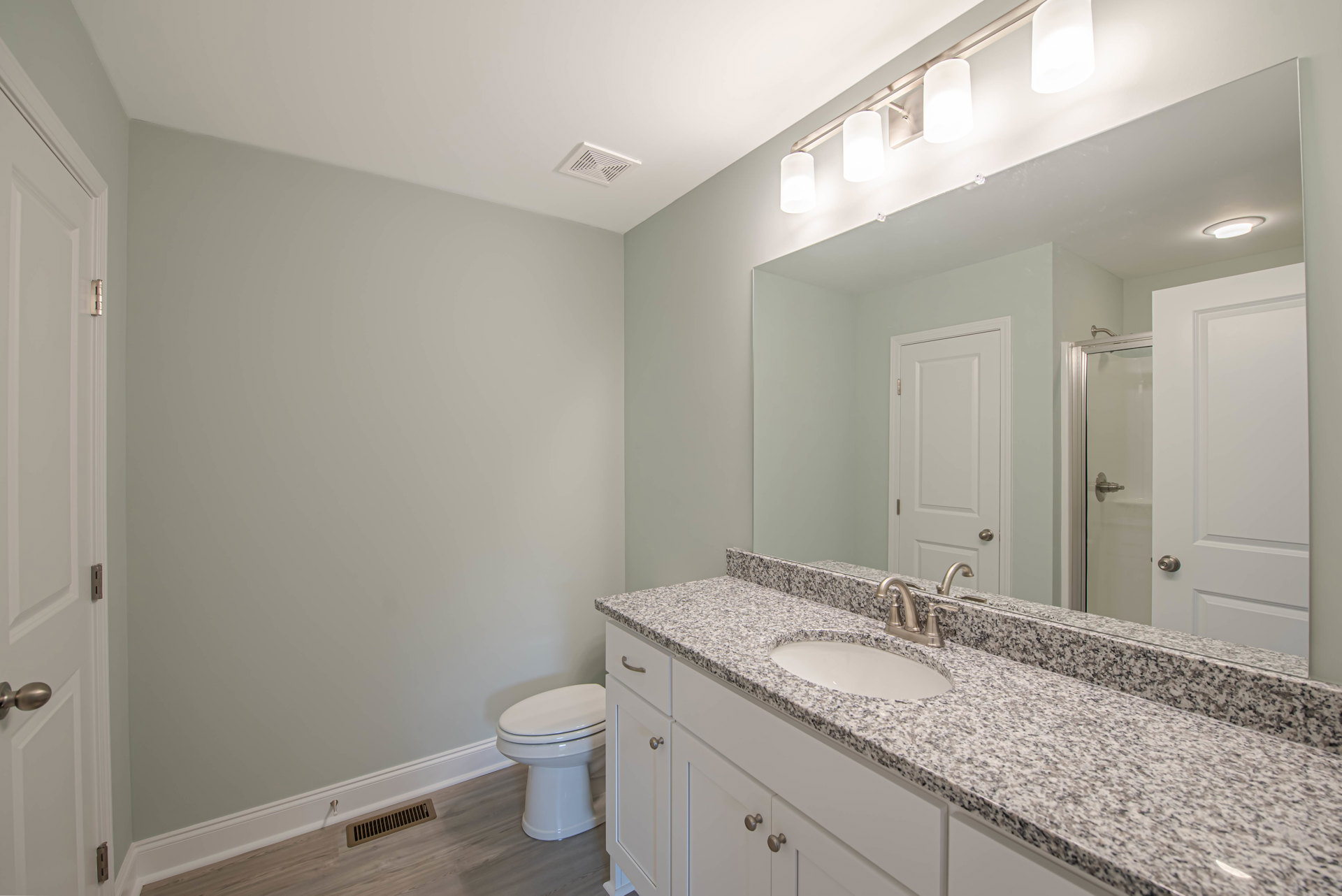 Marble countertop with undermount sink, chrome faucet, white toilet, wall-mounted mirror, light tile flooring, ceiling vent, white cabinetry