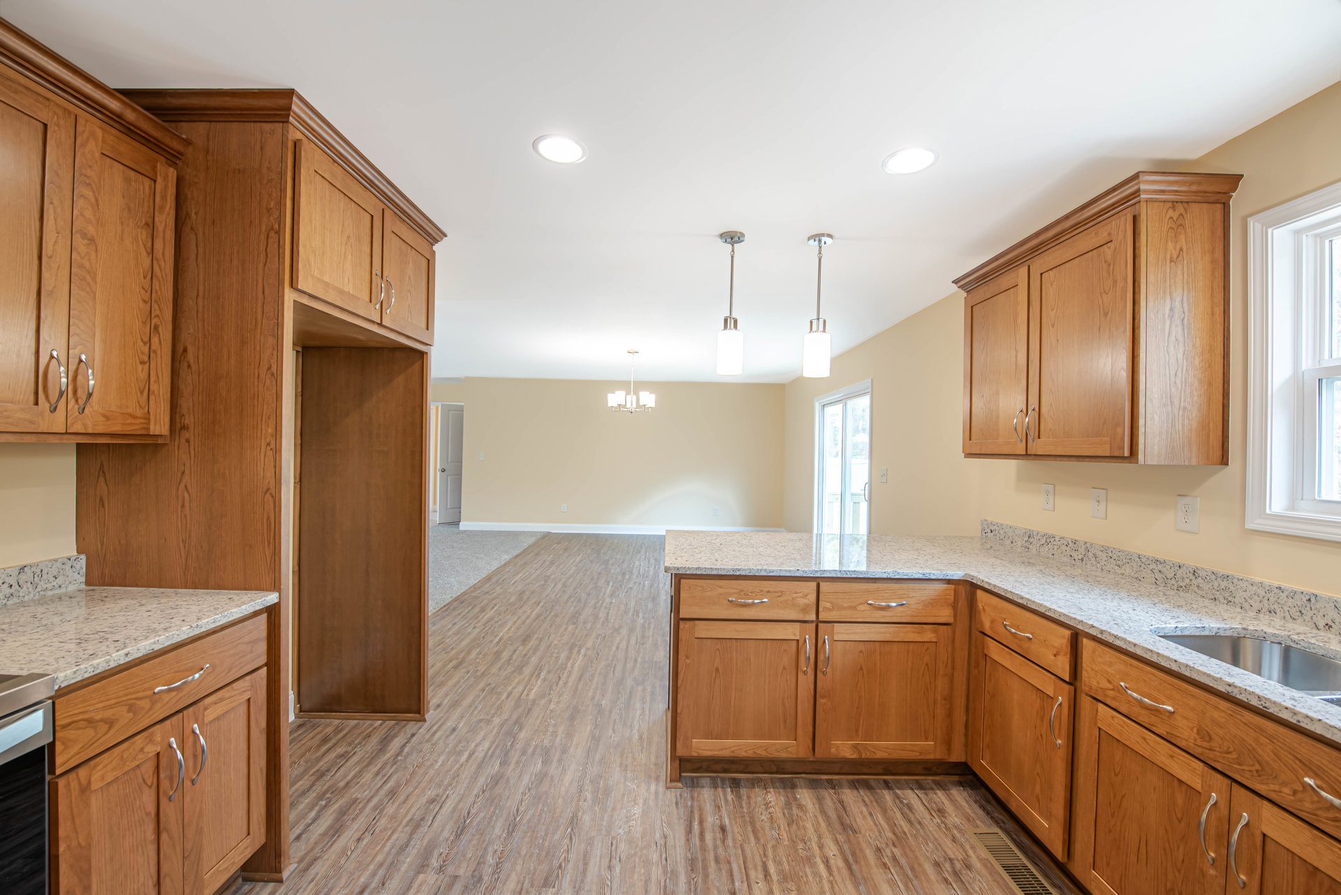Kitchen featuring wooden cabinets with silver handles, marble countertops, stainless steel sink, black cooktop, brown wooden door with white frame, and white window frame with