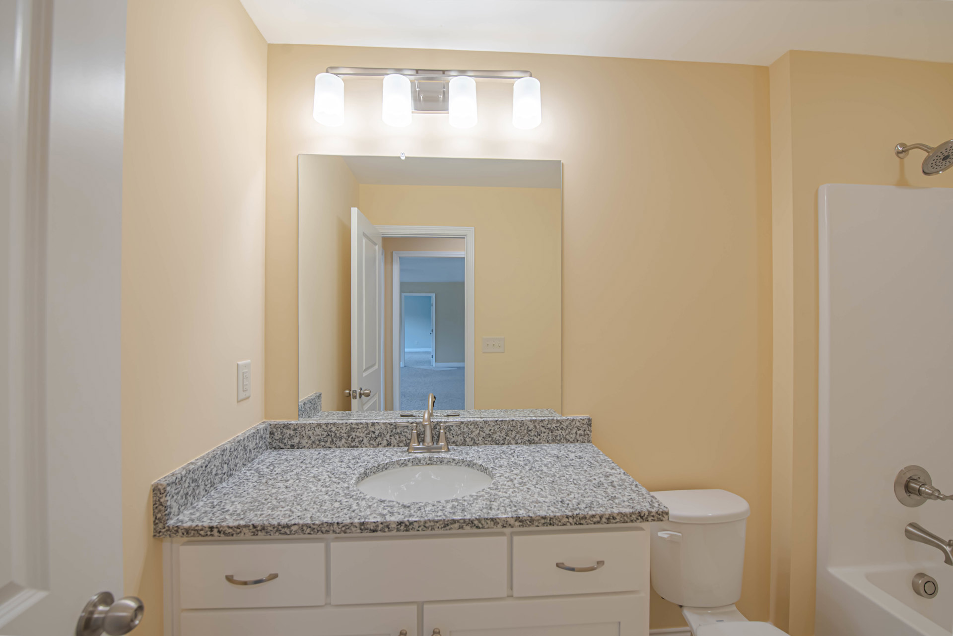 Marble bathroom countertop with undermount sink, chrome faucet, white toilet, light-colored tile backsplash, and white cabinetry