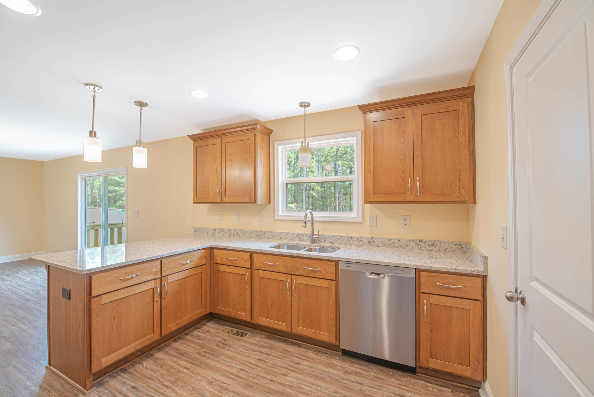 Wooden kitchen cabinets with brushed silver dishwasher, white quartz countertop, stainless steel sink, and natural light from window.