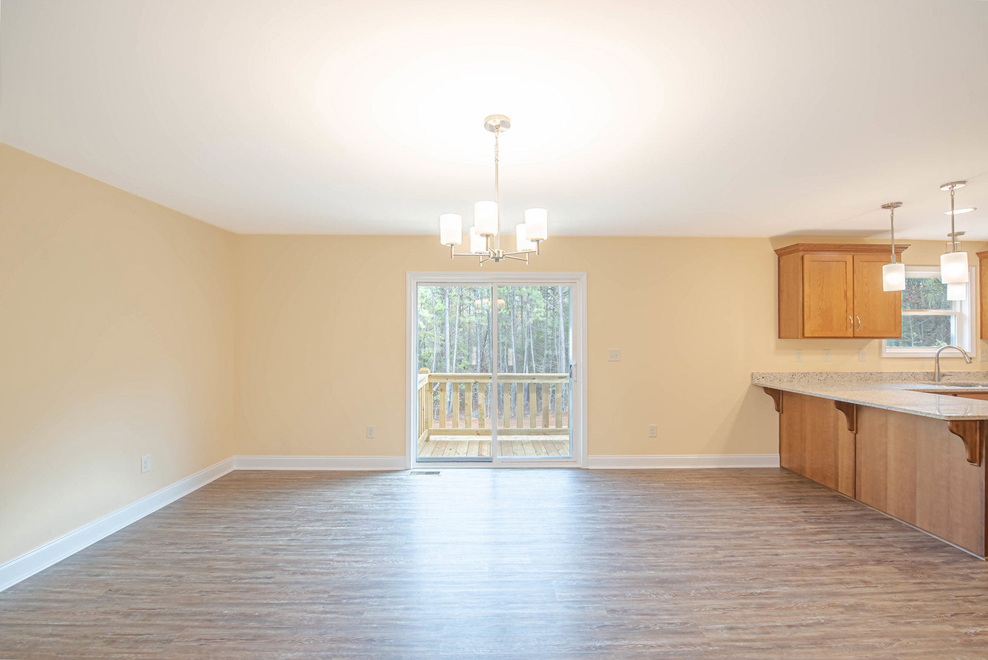 Open kitchen with white cabinetry, wood laminate flooring, sliding glass door leading to wooden deck, stone countertop, stainless steel sink, and recessed lighting