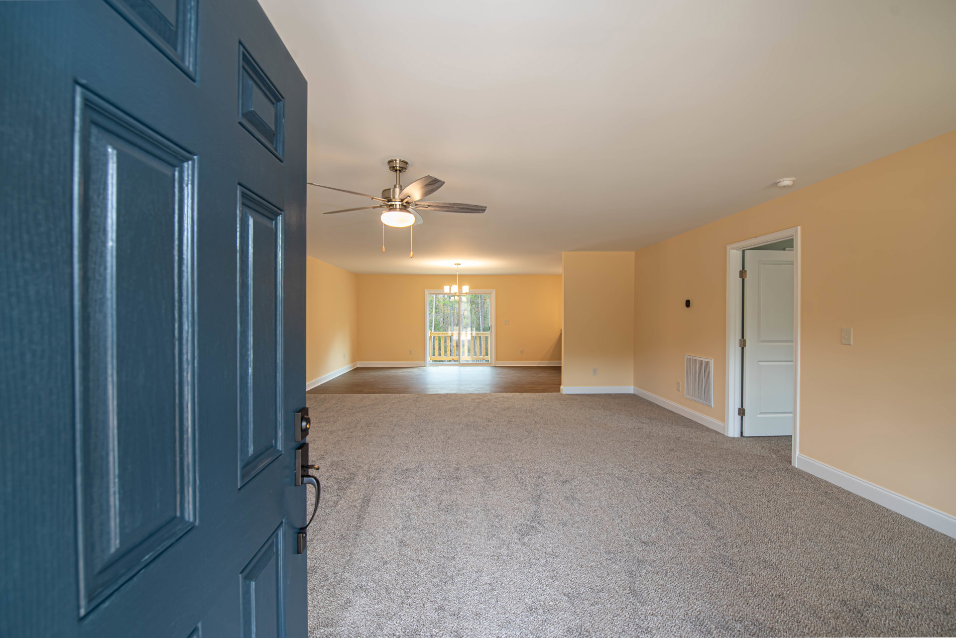 Carpeted bedroom with ceiling fan and light, white door with hinge, blue door, window overlooking trees, wall vent, plaster walls, and crown molding.