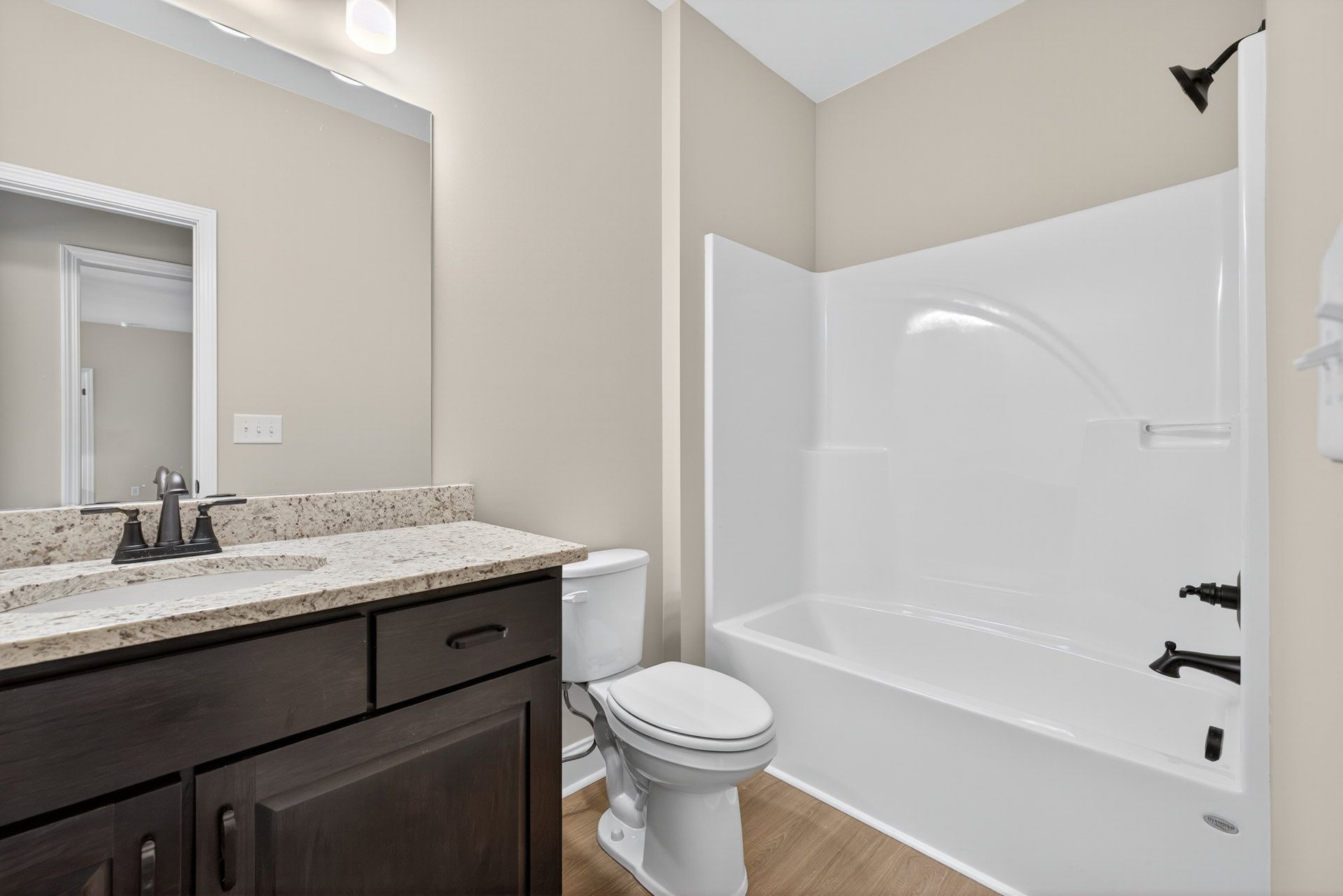 White bathroom with tile floor, white toilet with closed lid, built-in sink and faucet on light-colored countertop, wall-mounted mirror above sink, white door frame and door