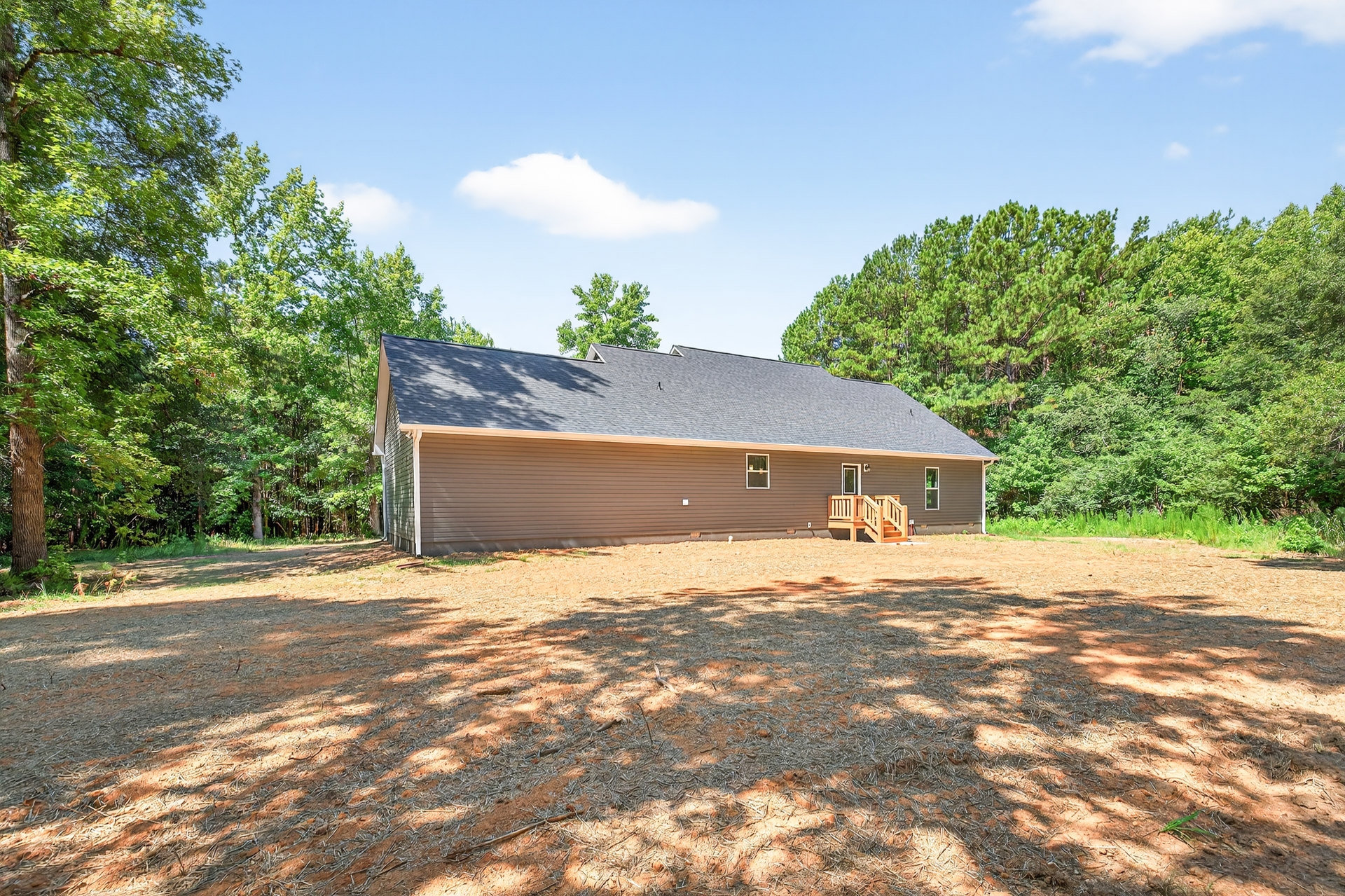 Two-story house with large windows and wooden porch railings, surrounded by tall trees and leafy branches on the ground, under a partly cloudy sky