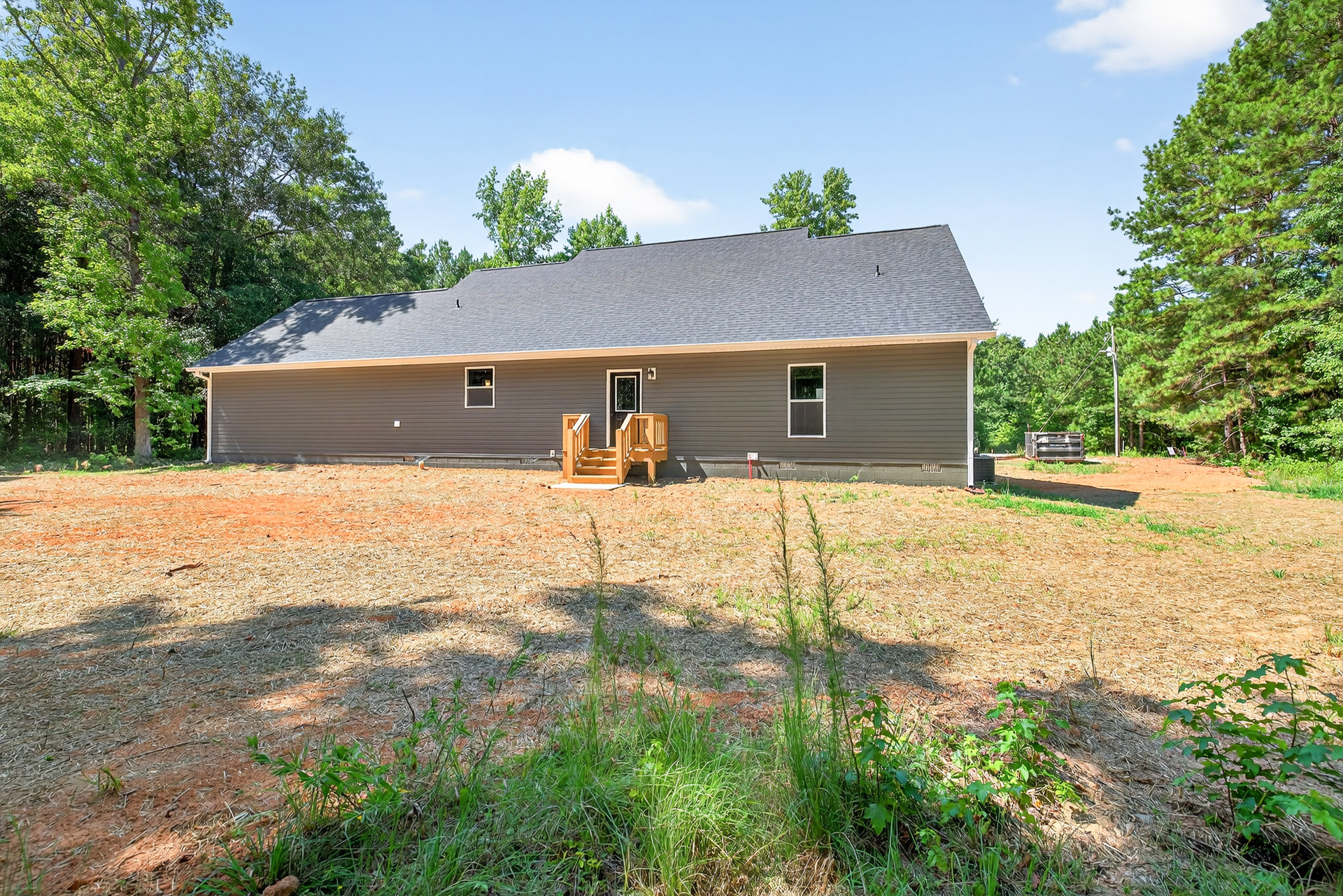 Two-story house with wood siding, large windows, and outdoor wooden staircase, surrounded by green lawn and leafy trees