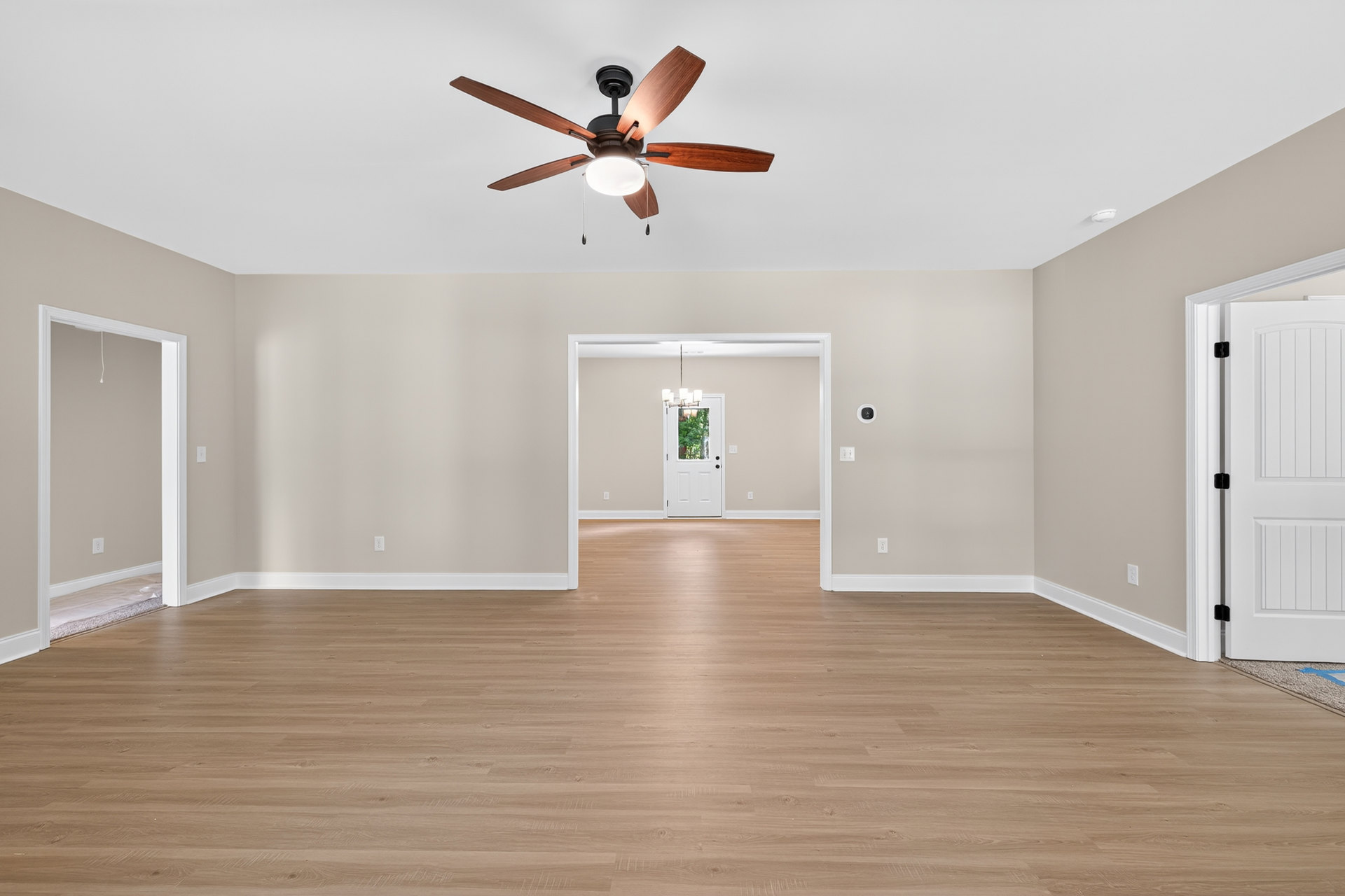 Ceiling fan with light fixture mounted on white ceiling above wood laminate flooring, white door with glass window and white trim, neutral walls in residential room.