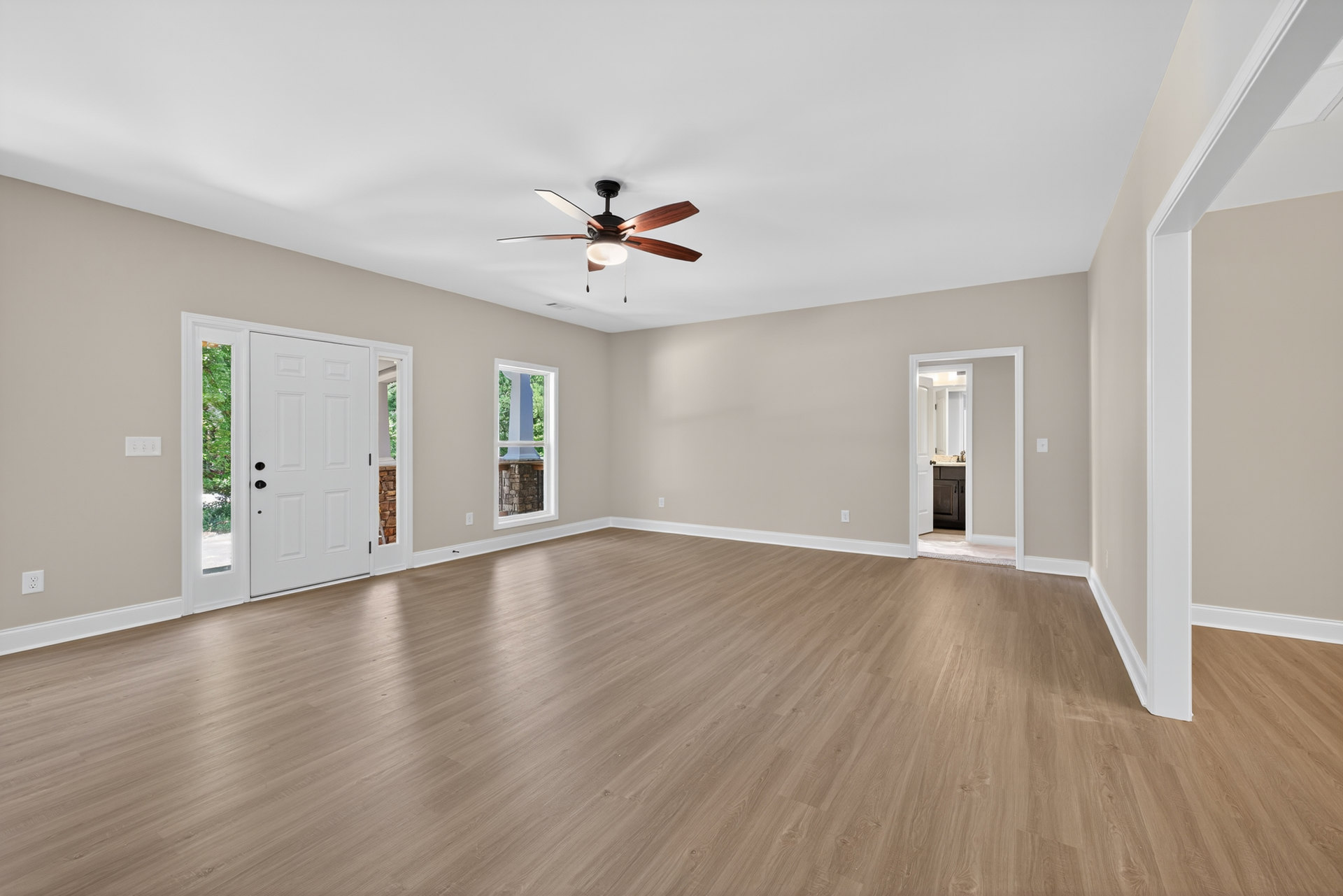 Ceiling fan with light fixture, wood flooring, white walls, window with white trim, glass-paneled door, partial view of bathroom with dual sinks