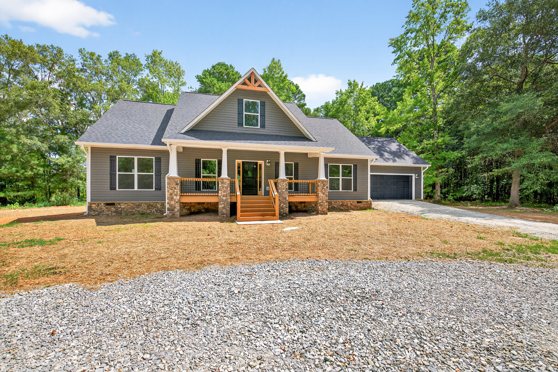 Two-story house with white siding, black glass-paneled front door, wooden porch and deck, white-framed windows, concrete driveway, and landscaped yard with trees.
