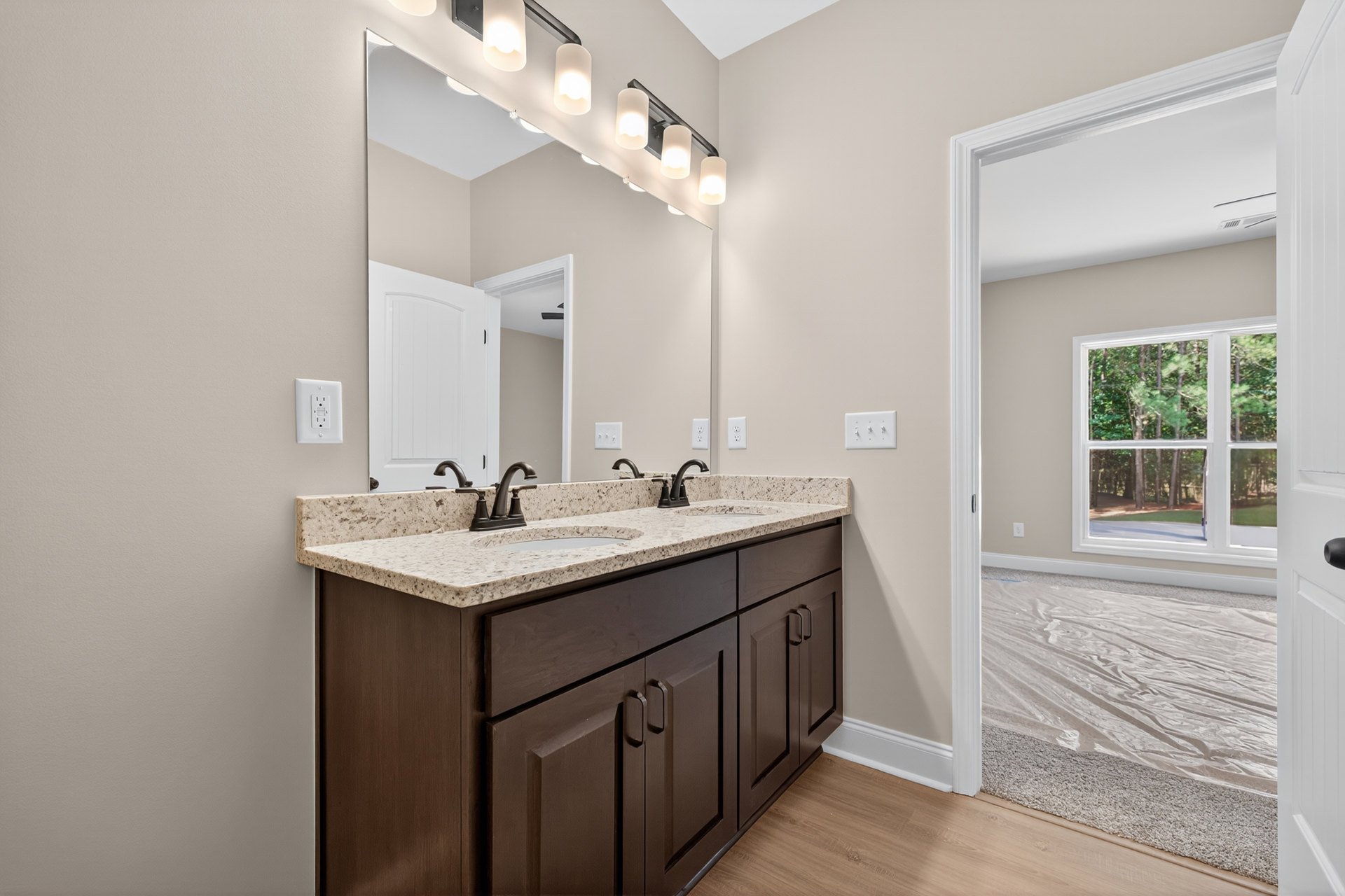 Bathroom with double sink vanity, large mirror, white tile backsplash, light wood cabinetry, and window overlooking trees.