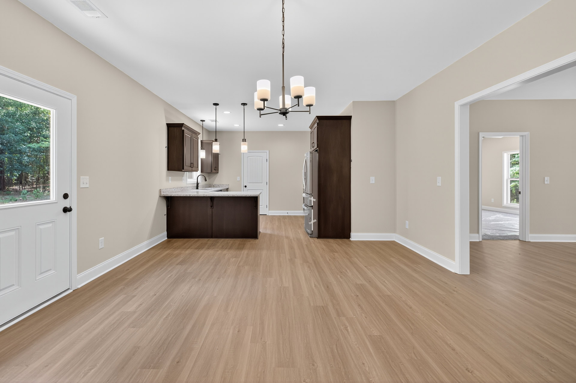 Open kitchen and dining area featuring hardwood floors, white cabinetry, marble countertop, stainless steel refrigerator, and a white door with window; green tree with white