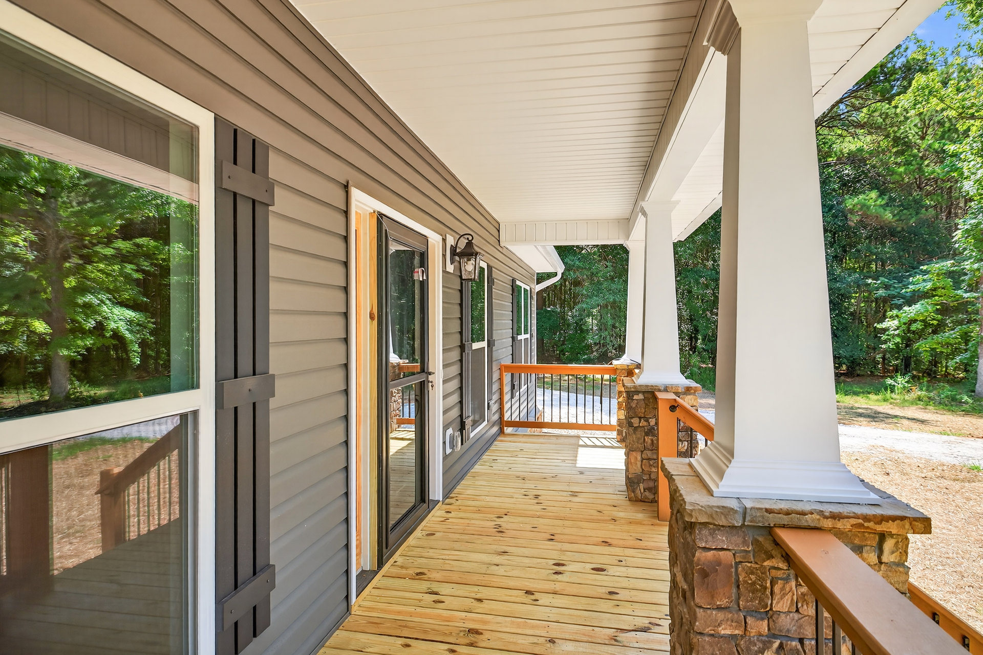 Stone railing and wall on a wooden porch, glass door entry, shaded by nearby trees and plants