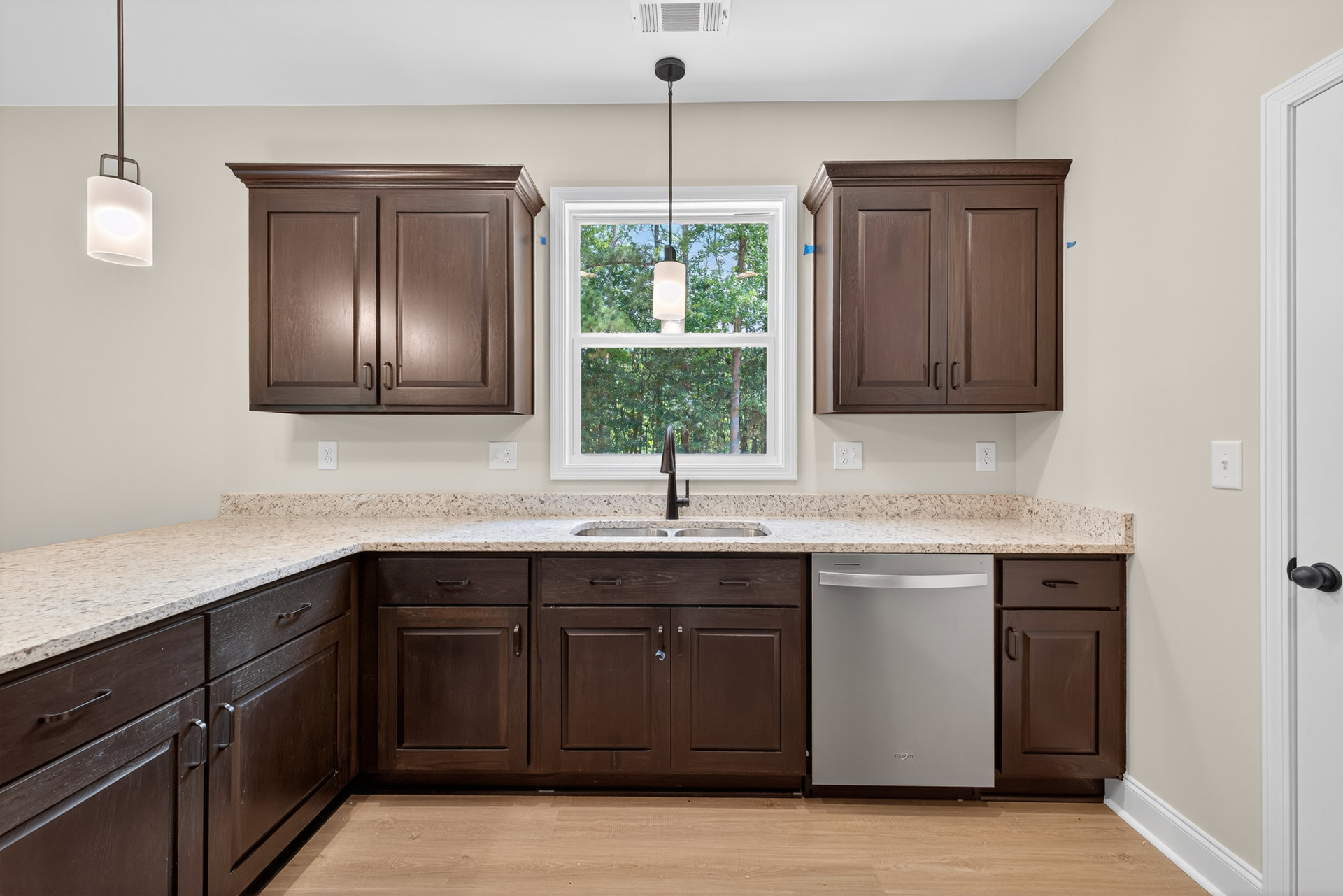 Dark wood kitchen cabinets, stainless steel sink, silver refrigerator with handle, sunlight streaming through window, blue object mounted on wall cabinet, person holding phone