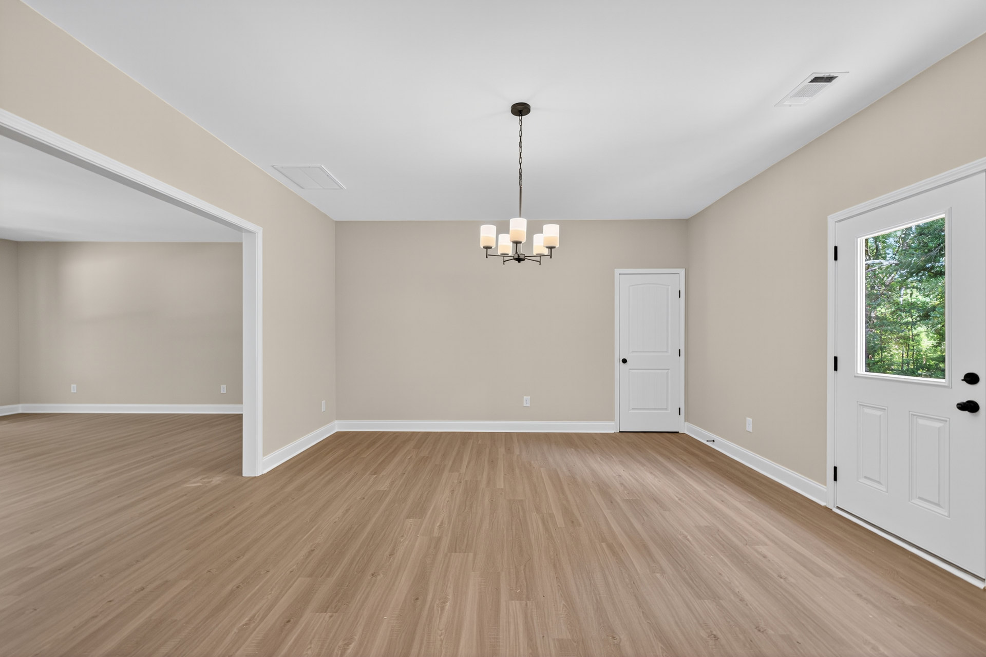 Wood floor with white trim, white doors featuring black hardware and window panes, chandelier with glass accents hanging from plaster ceiling, large window framing leafy trees