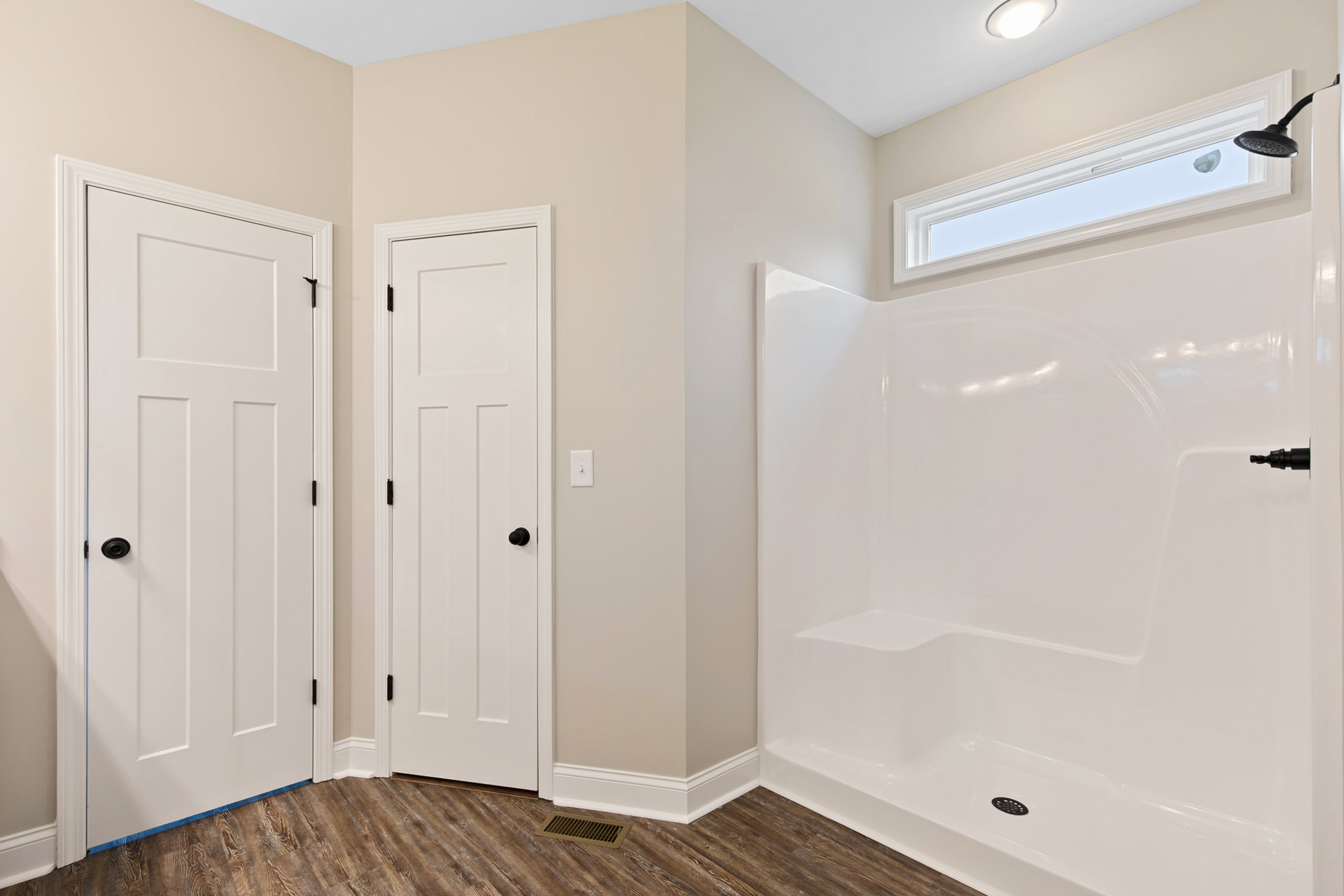 Bathroom with white walls, white shower enclosure, white door featuring black handle, wall vent, and light-colored flooring