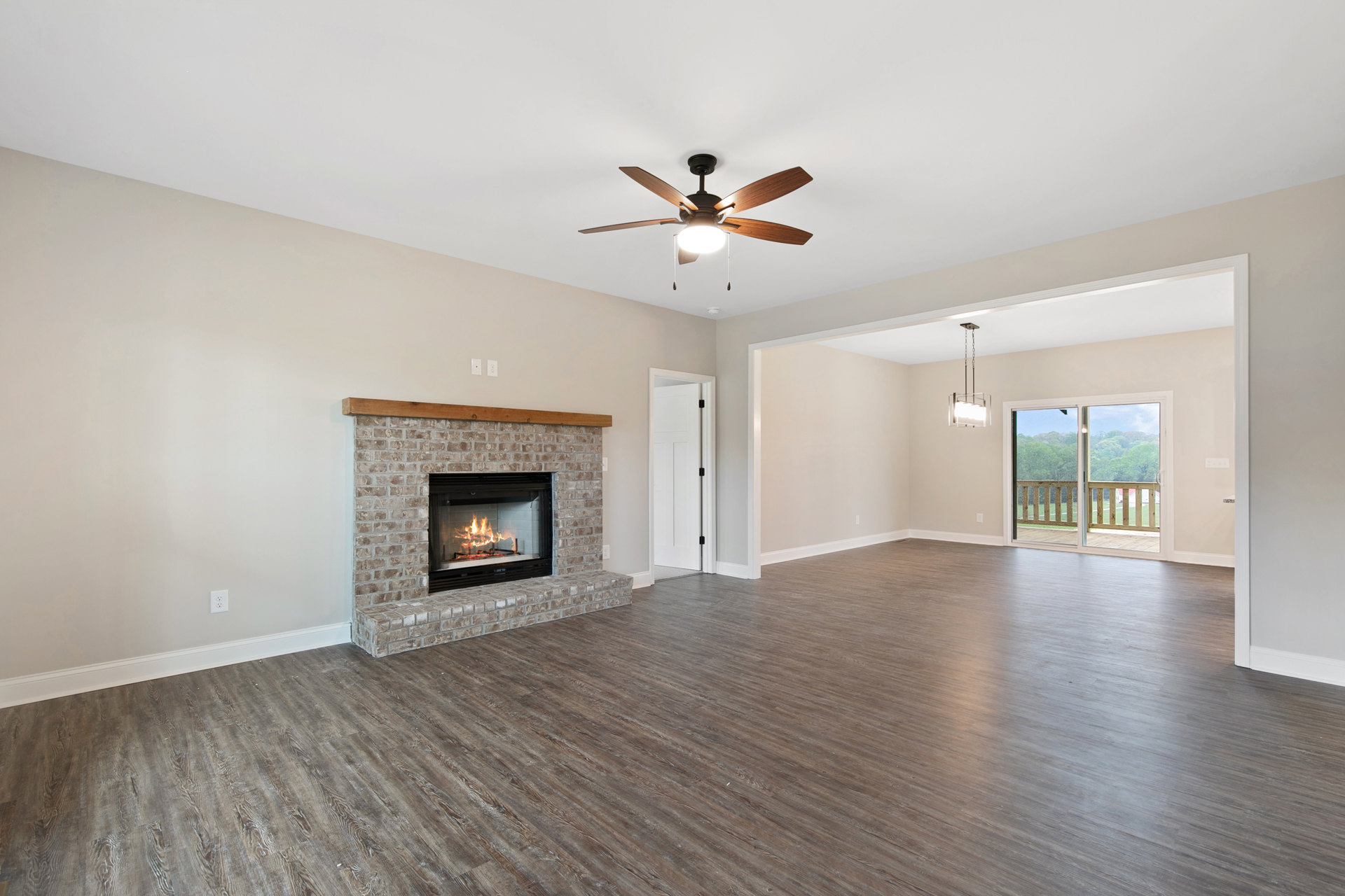 Living room with wood flooring, stone fireplace with wood mantel, ceiling fan with light, sliding glass door opening to deck