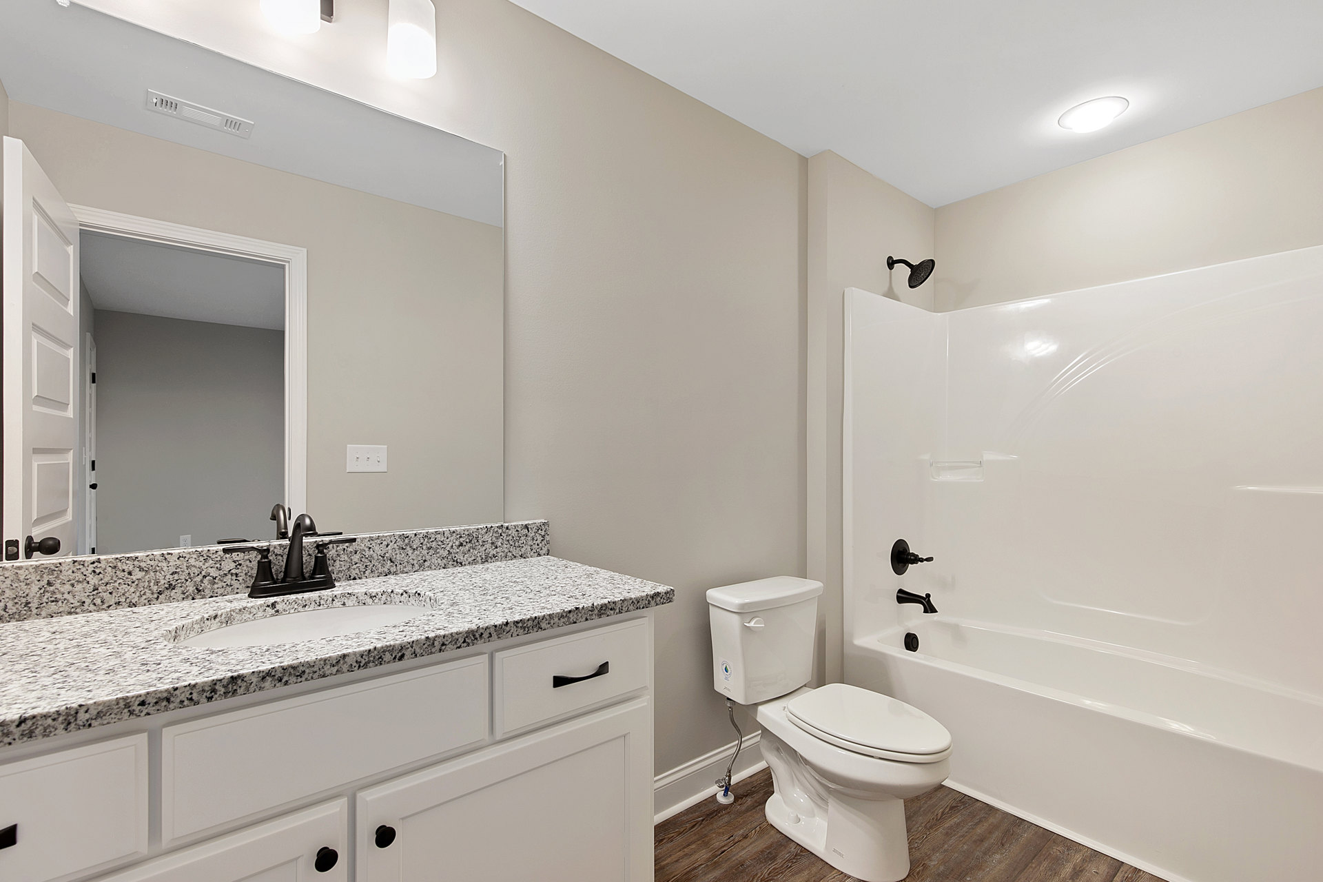 Modern bathroom featuring a white toilet, rectangular sink with chrome faucet, light-colored tile walls, large mirror, and stone countertop