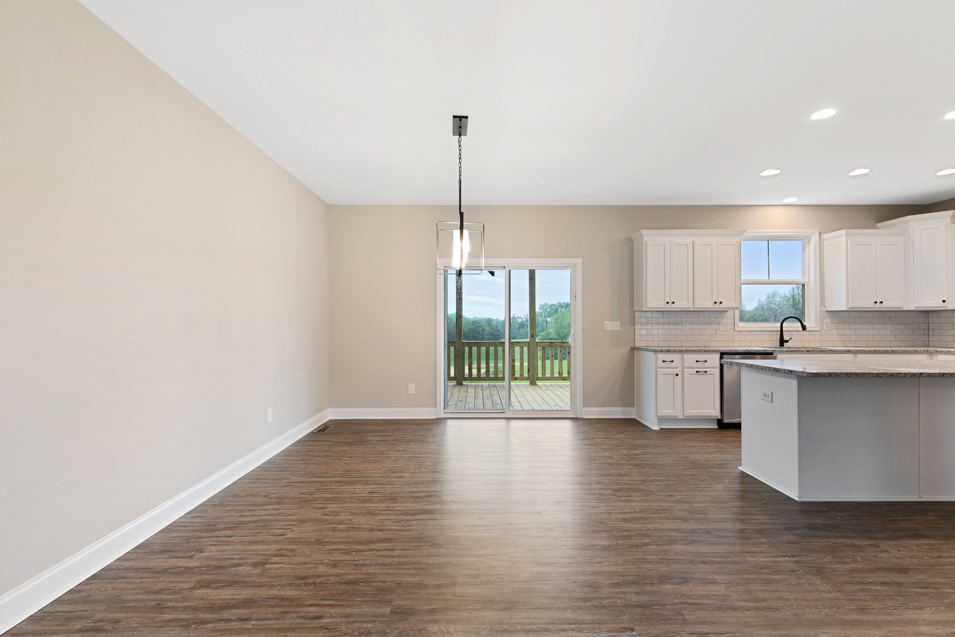 Hardwood floor kitchen and dining area featuring a white island with granite countertops, black faucet beneath a window, sliding glass door opening to a wooden deck with matching