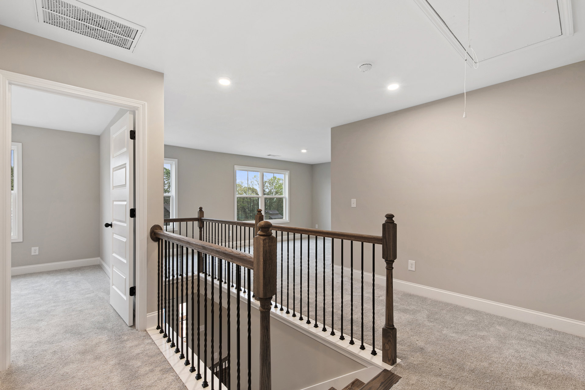 Wood staircase with matching handrail and balusters, plaster walls, vent in ceiling, large window overlooking trees, hardwood flooring