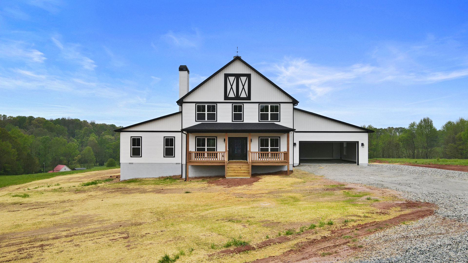 White two-story house with black-framed windows, wooden steps leading to a black front door, expansive driveway, manicured lawn, chimney, and surrounding trees under a partly