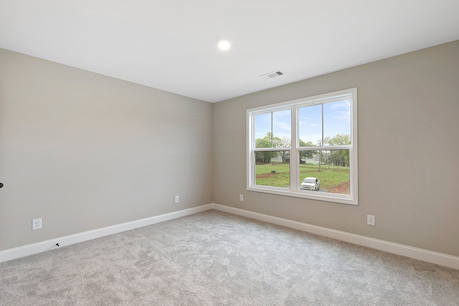 Carpeted room with white walls, large window, and ceiling light fixture; parked white truck visible outside through the window.