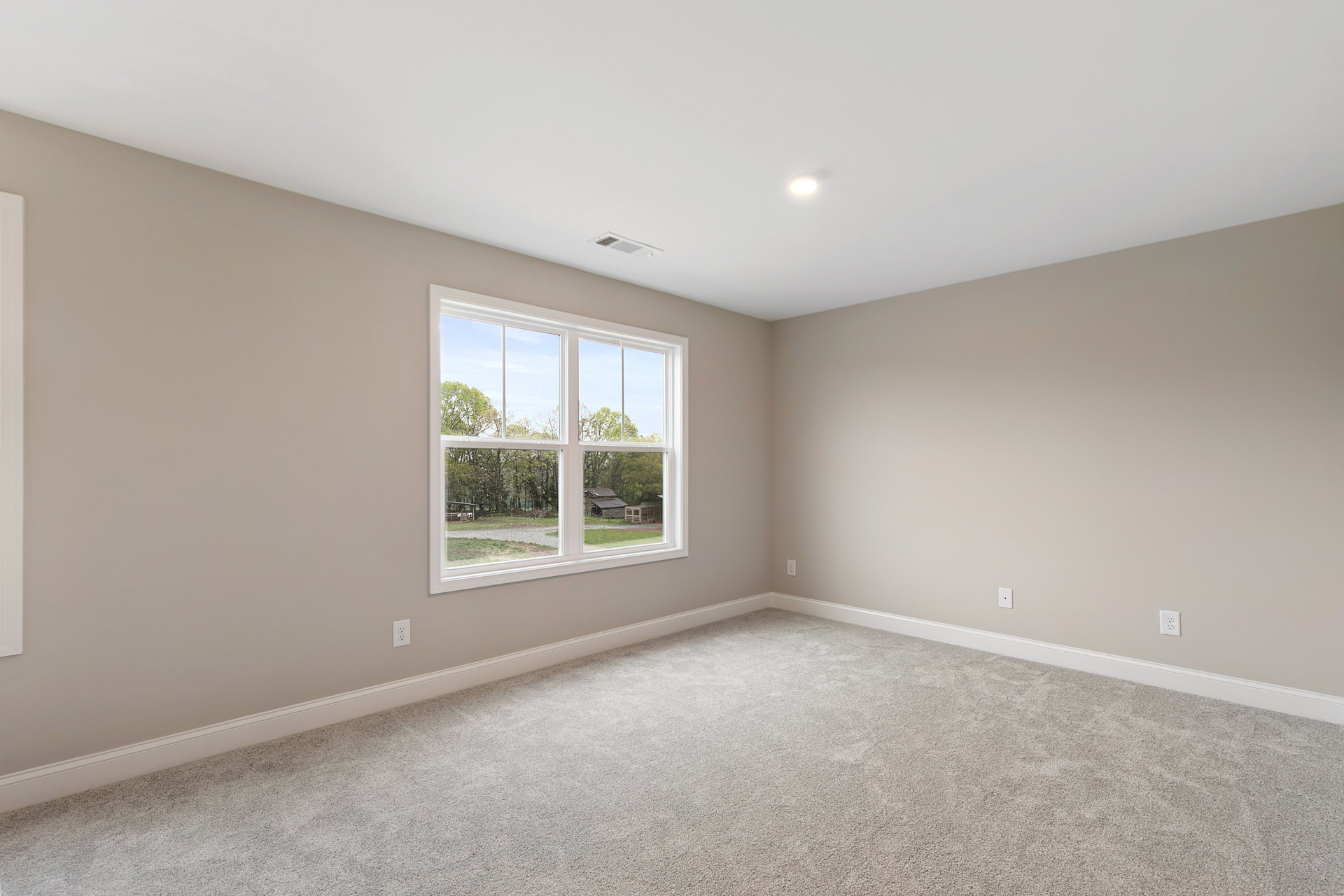 Carpeted bedroom with white walls, large window overlooking yard and trees, ceiling vent and recessed light fixture