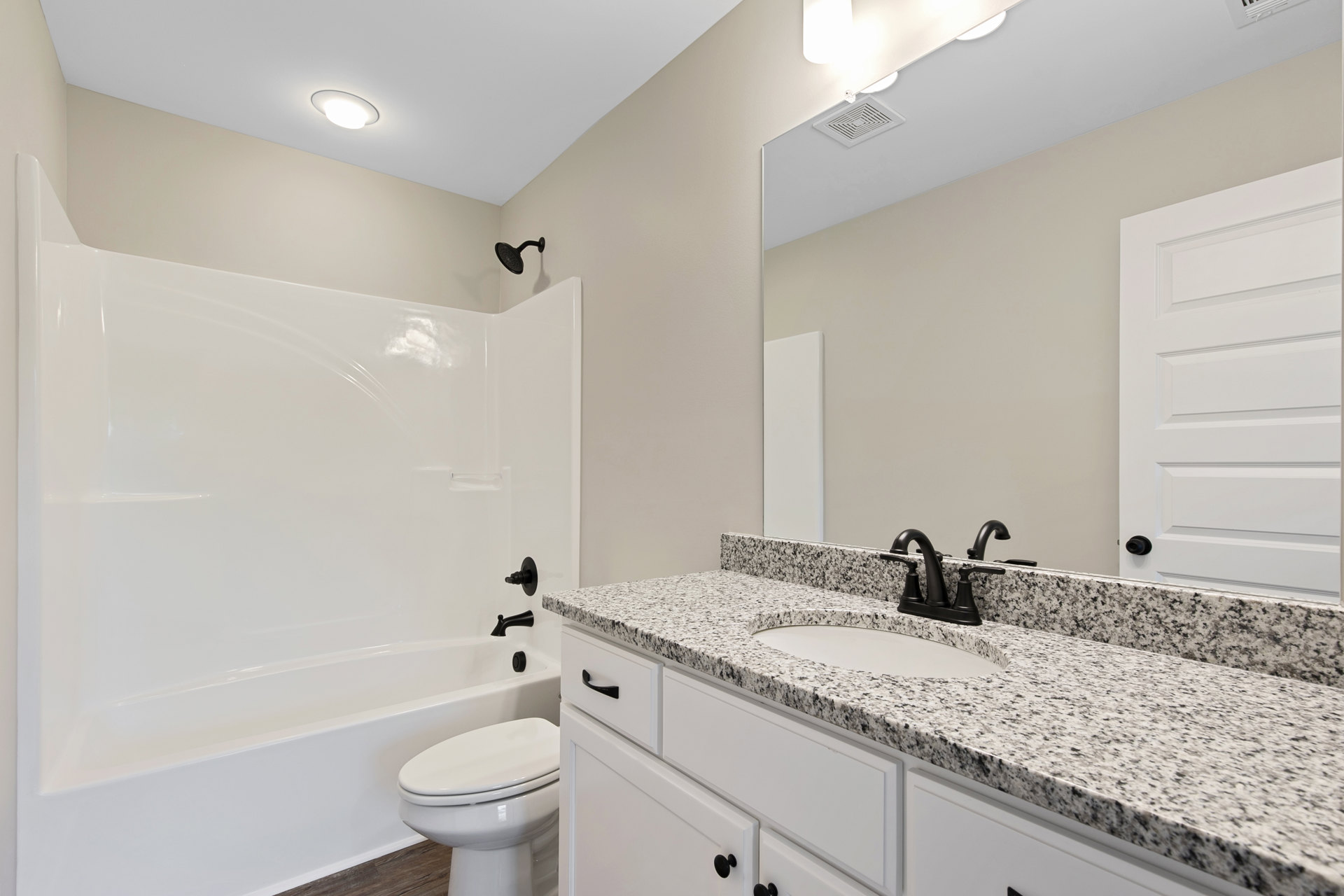 Modern bathroom featuring a white porcelain sink with chrome faucet, white toilet, glass-enclosed shower with black shower arm, light tile flooring, and white painted door.