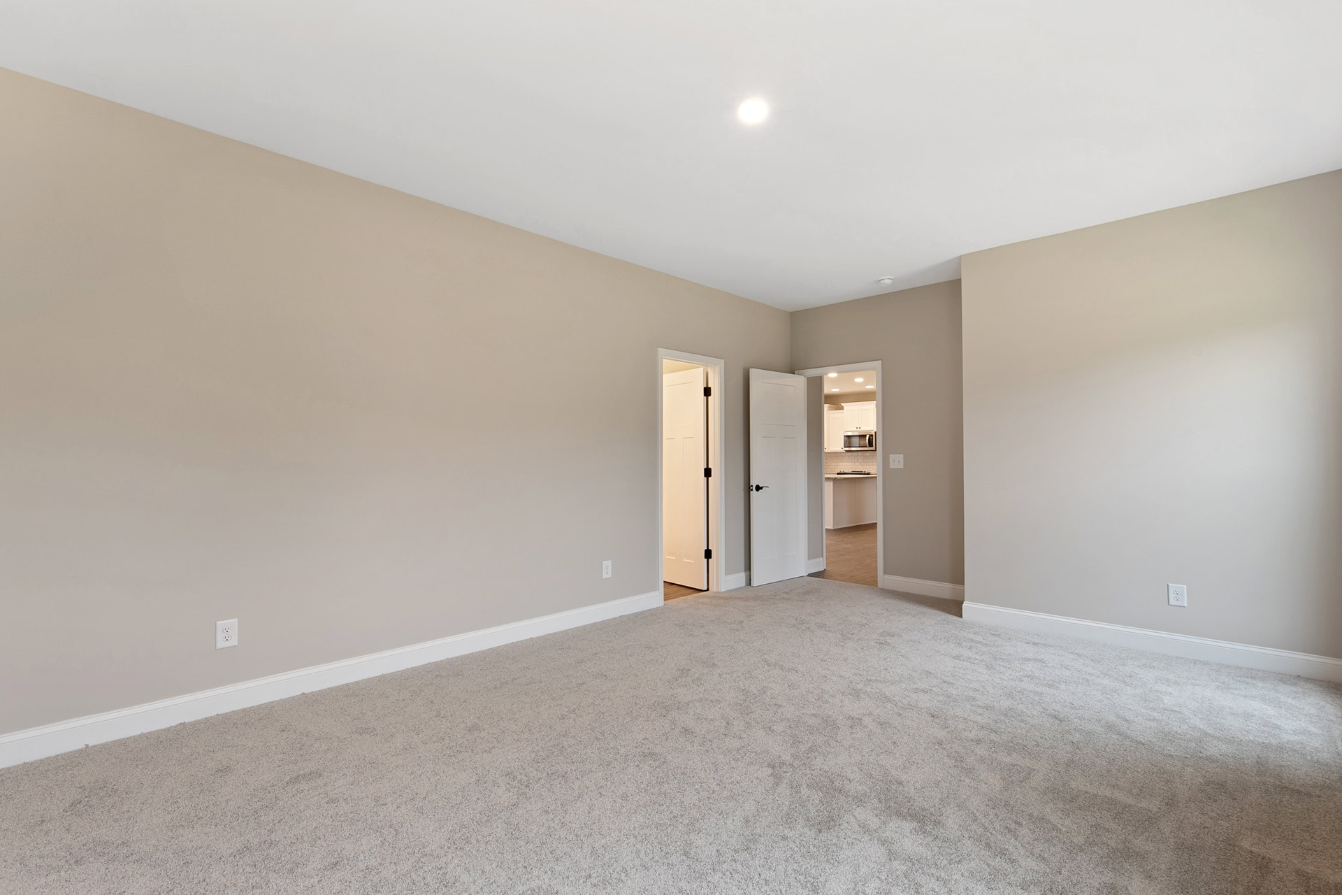 Beige carpeted room with white walls, white door featuring a black handle, open doorway, simple ceiling, and minimal molding