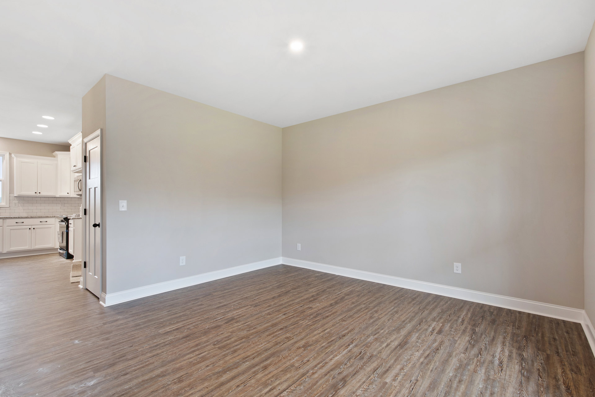 Open white door leading into a room with hardwood floors, white walls, and white trim, illuminated by natural light.