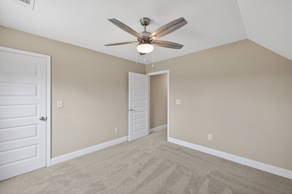 Ceiling fan with light fixture above carpeted floor, white door with silver handle, neutral walls and crown molding