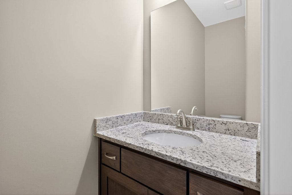 Marble bathroom countertop with undermount sink, chrome faucet, white cabinetry, and tile backsplash