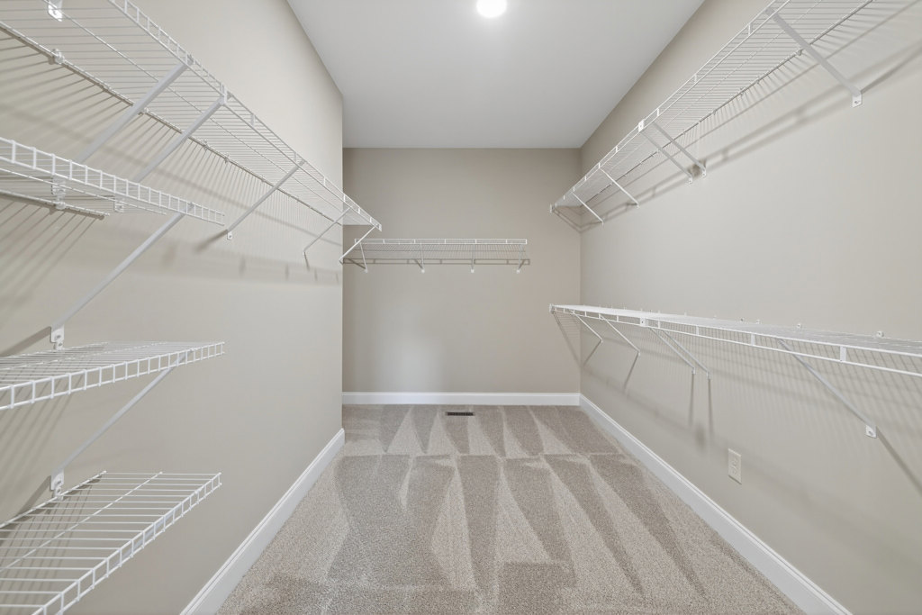 Walk-in closet with white wire shelving on walls, carpeted floor with air vent, white painted walls and baseboard molding