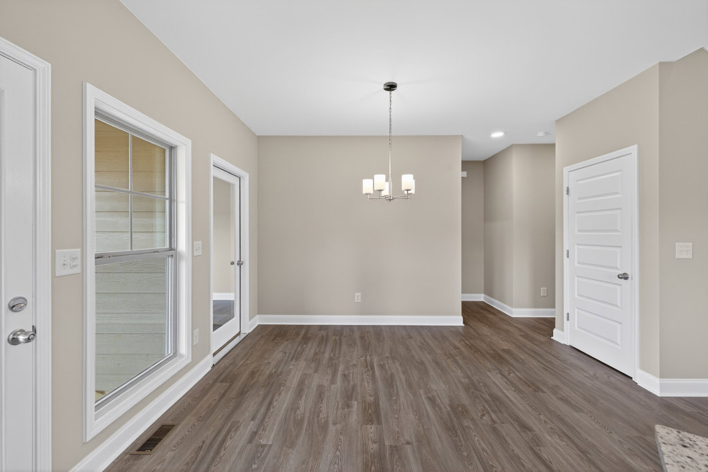 Wood flooring in a bright room with a modern chandelier, white paneled door with silver handle, and large window framed by plaster walls