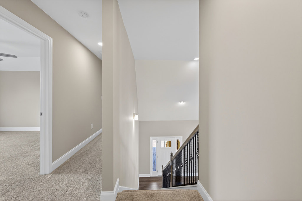 Hallway with white walls, carpeted floor, black metal stair railing, and white door with trim molding