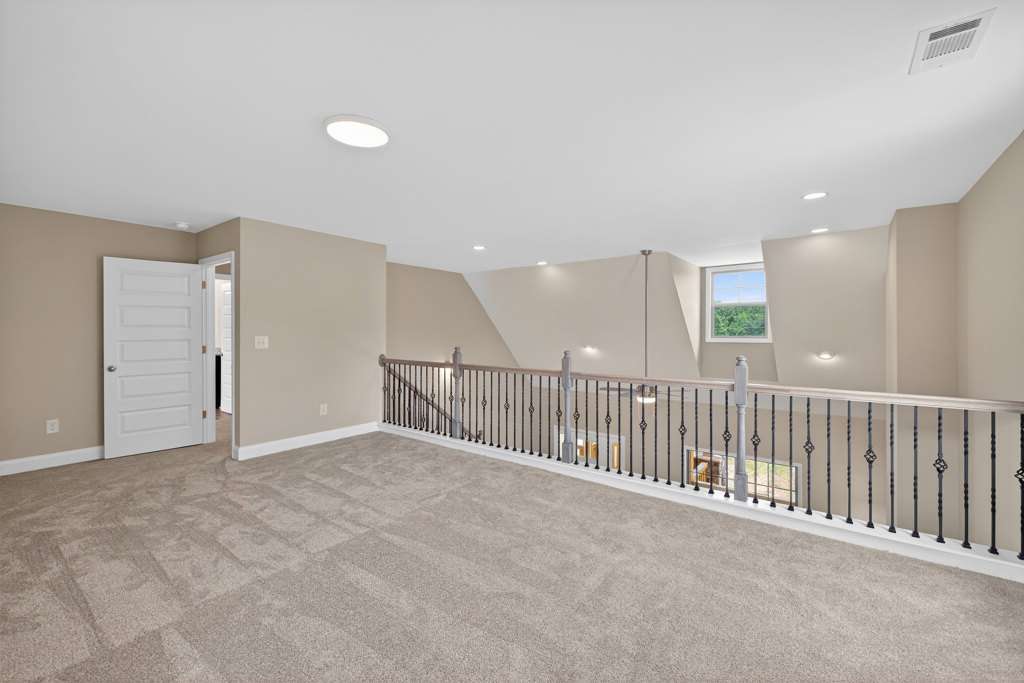 Carpeted room featuring a white staircase with metal railing, white door with silver handle, large window overlooking trees, and white ceiling with recessed lighting