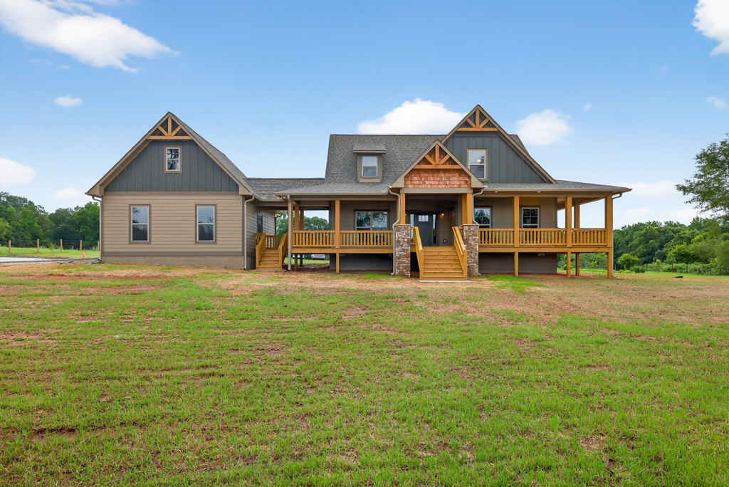 Two-story house with covered front porch, yellow steps, attached garage, expansive green lawn, mature trees, and partly cloudy sky