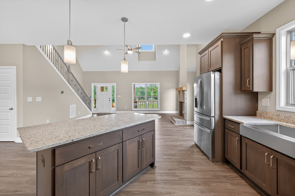 Spacious kitchen featuring a marble-topped island, tile flooring, white cabinetry, stainless steel refrigerator, fireplace with stone surround, and a window overlooking a fenced