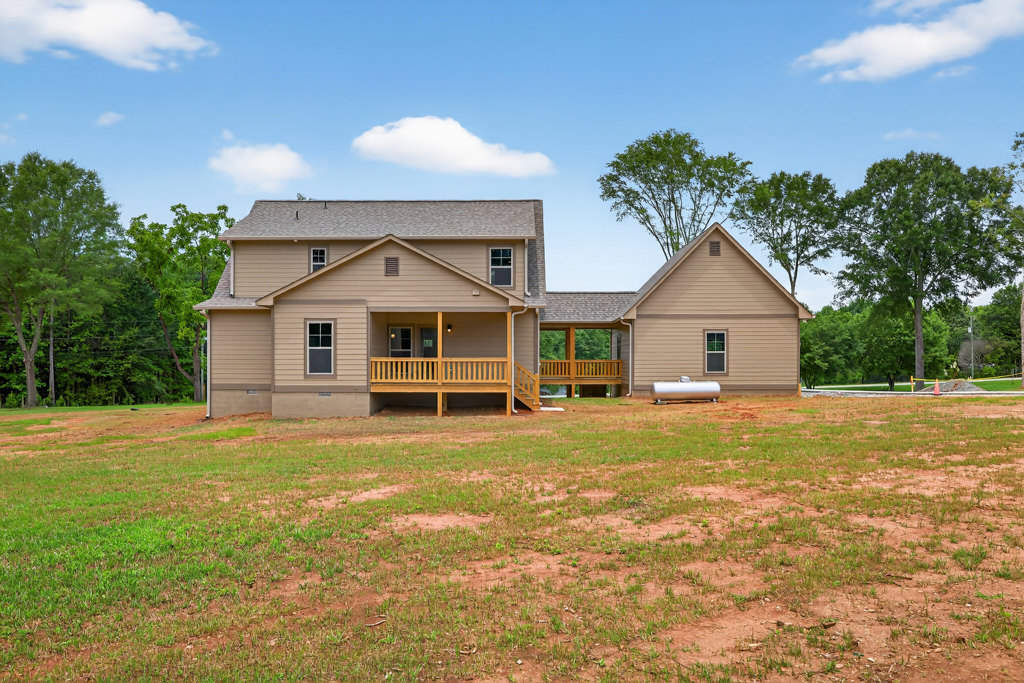 Two-story house with large windows, wooden deck and railing, surrounded by a spacious grassy yard, trees, and a partly cloudy sky