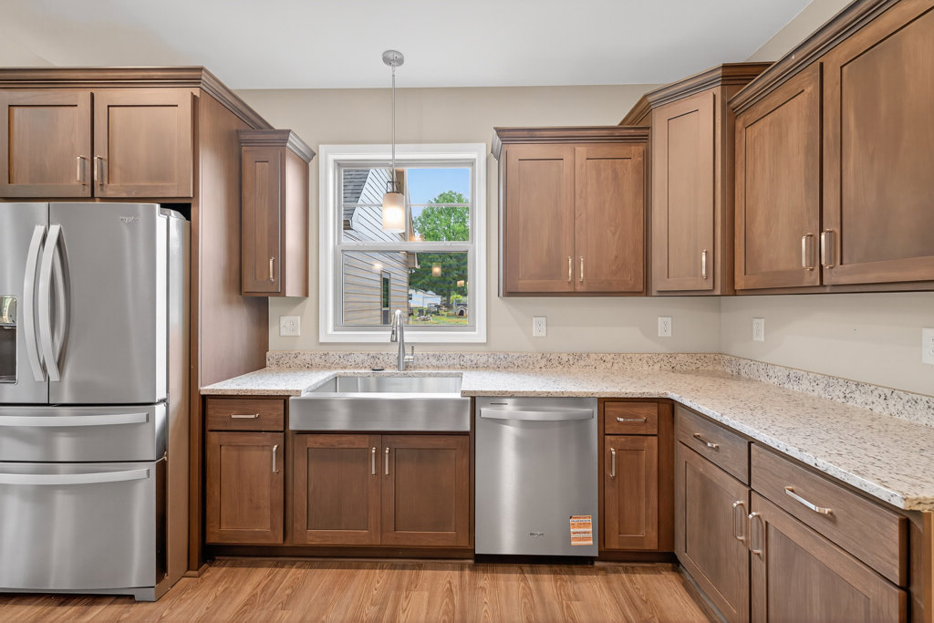 Granite countertops with stainless steel sink, silver dishwasher, stainless refrigerator, white cabinetry, and window providing natural light