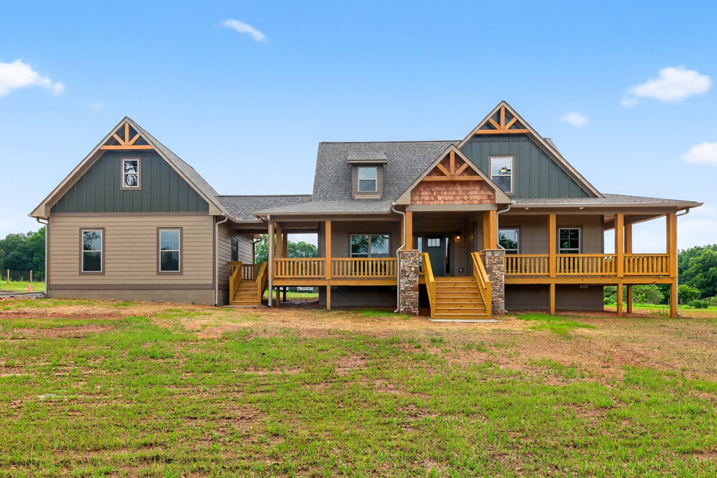White cottage-style house with covered front porch, yellow steps, manicured green lawn, mature tree, and cloudy sky backdrop