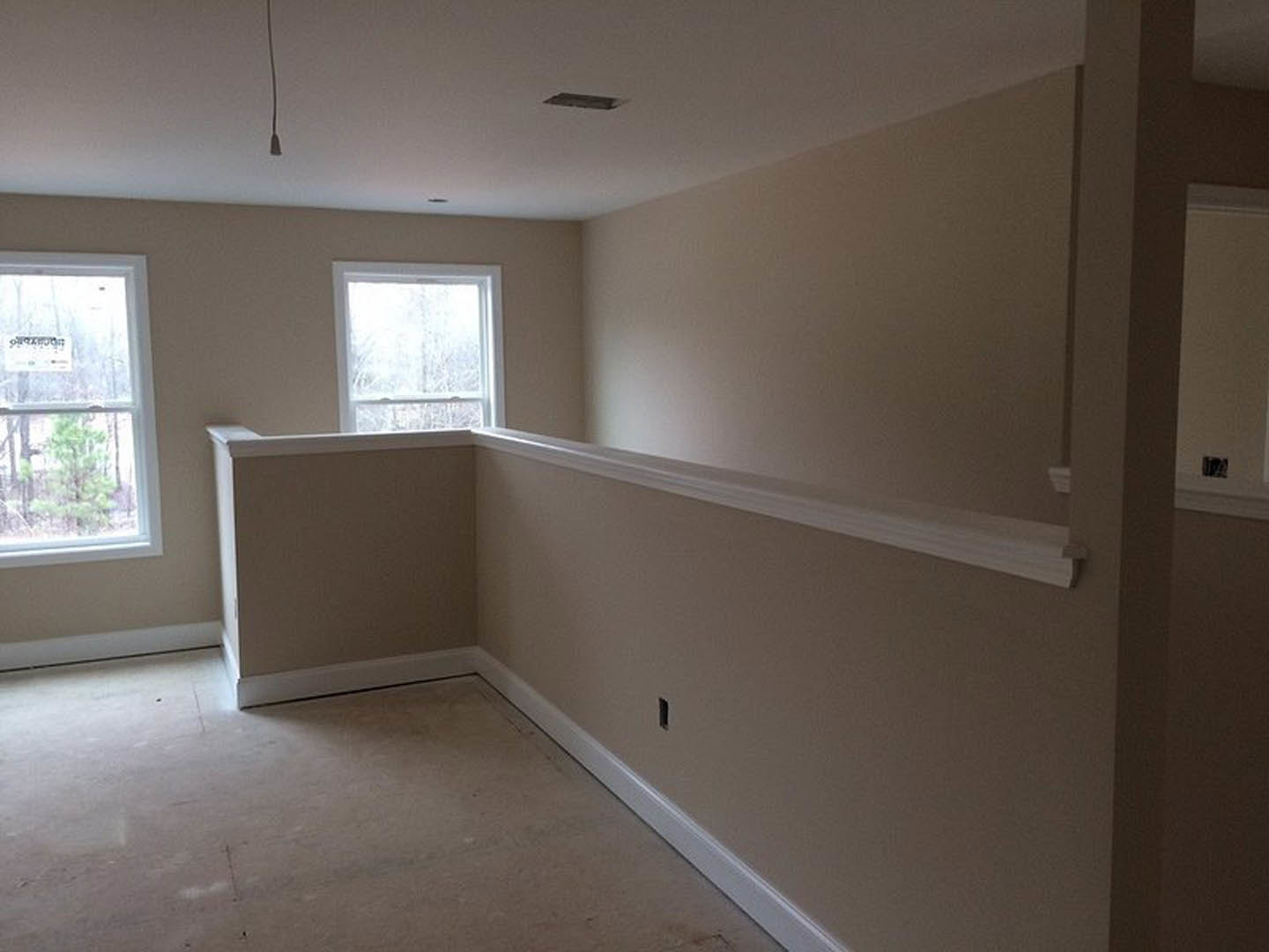 Sunlit room featuring a white-framed window with a sign, white wall with decorative molding, and light reflecting on hardwood flooring.