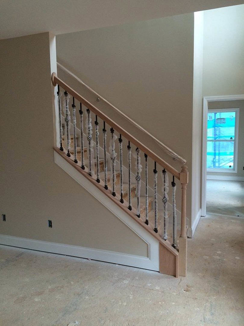 Wood staircase with white balusters and wooden handrail, blue curtained window, white floor, and white table in a bright residential interior