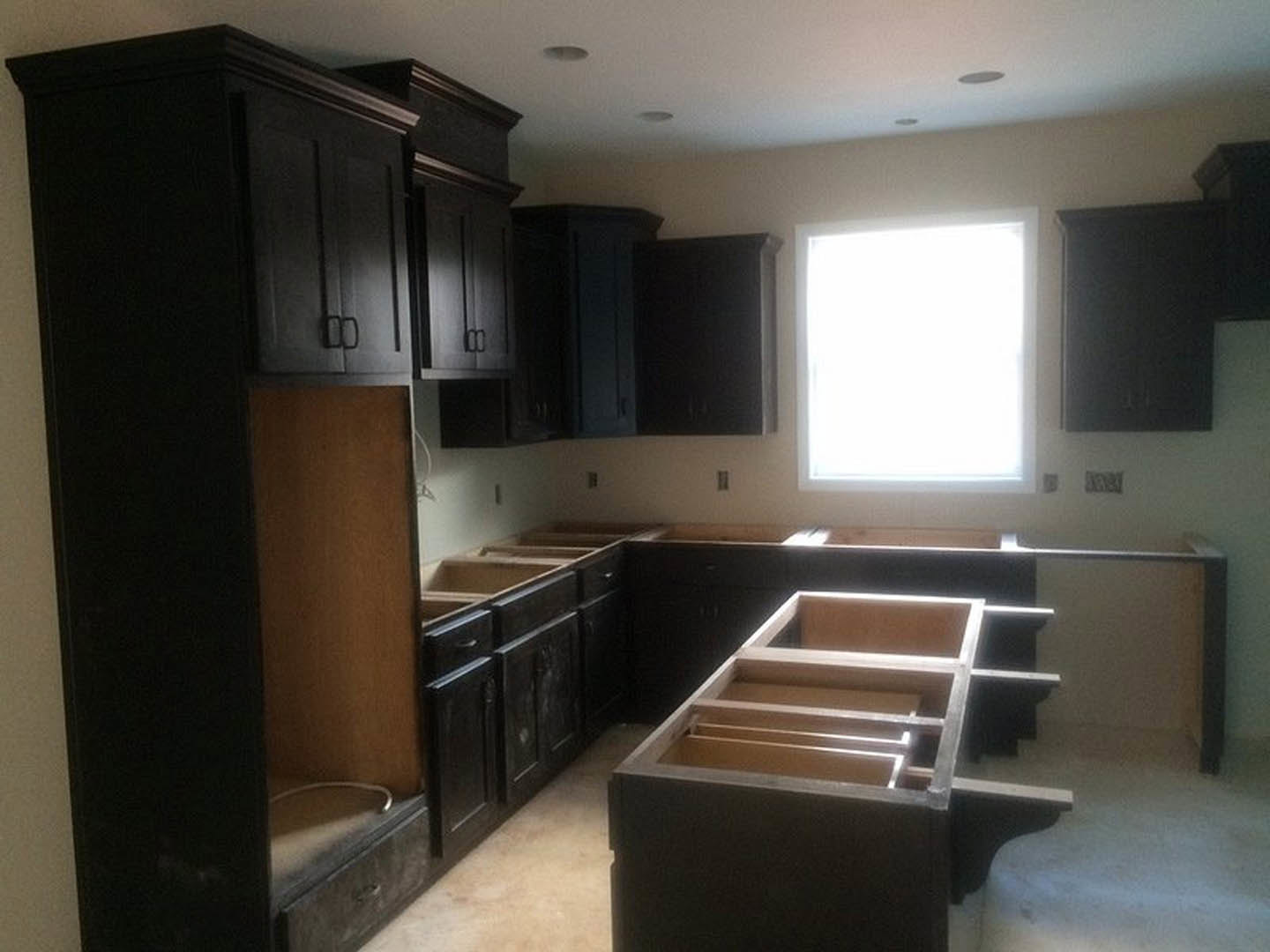 Dark wood kitchen cabinets, white rectangular window with bright natural light, wooden shelf box, close-up of drawer, brown wall with exposed metal pipe, light-colored flooring
