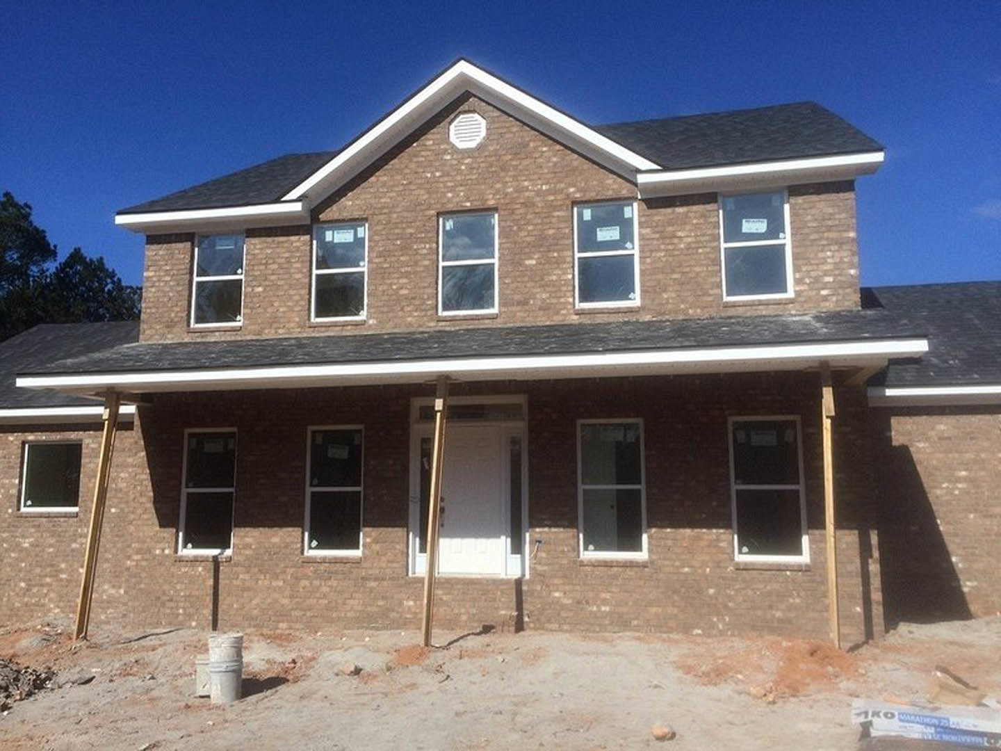 Partially constructed brick house exterior with white framed window, white door with gold trim, white vent, and exposed white pipe