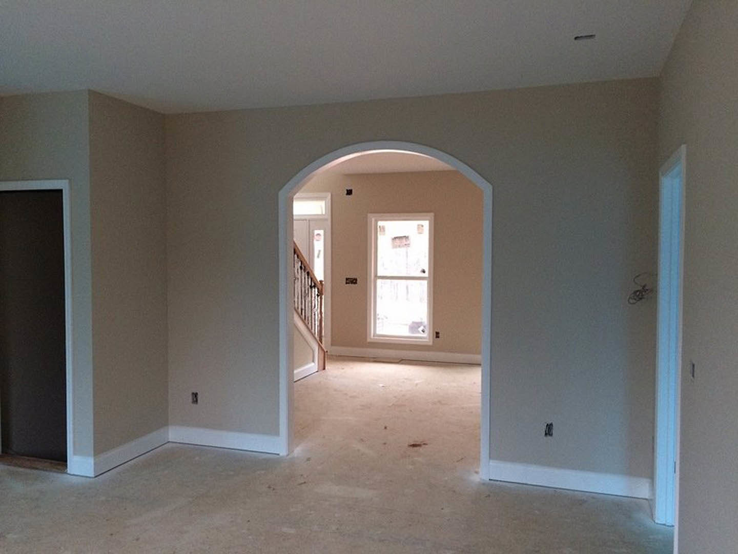 Open white door with sign, black accent wall with white trim, staircase partially visible, light-colored flooring, white ceiling with crown molding.