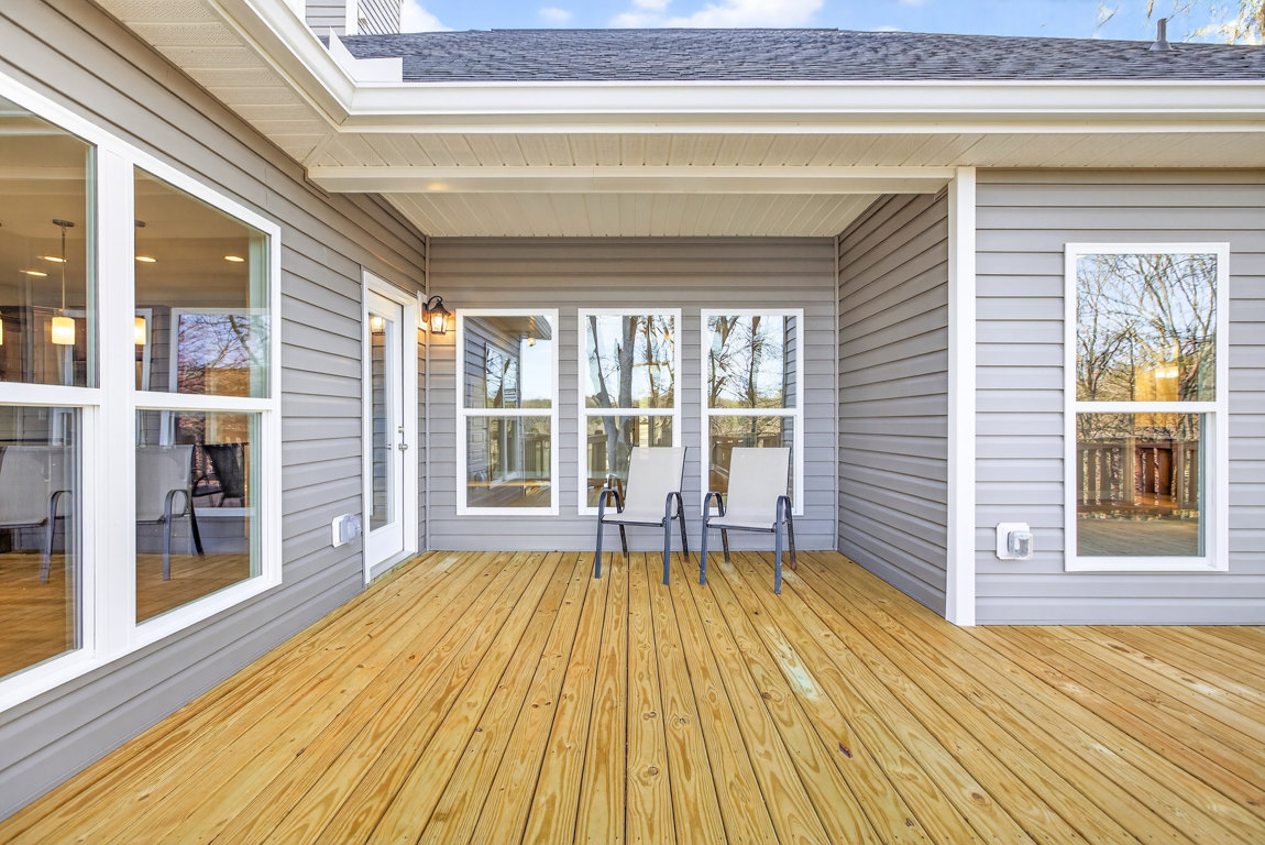 Wood deck with two white chairs, large window overlooking trees, and natural wood flooring